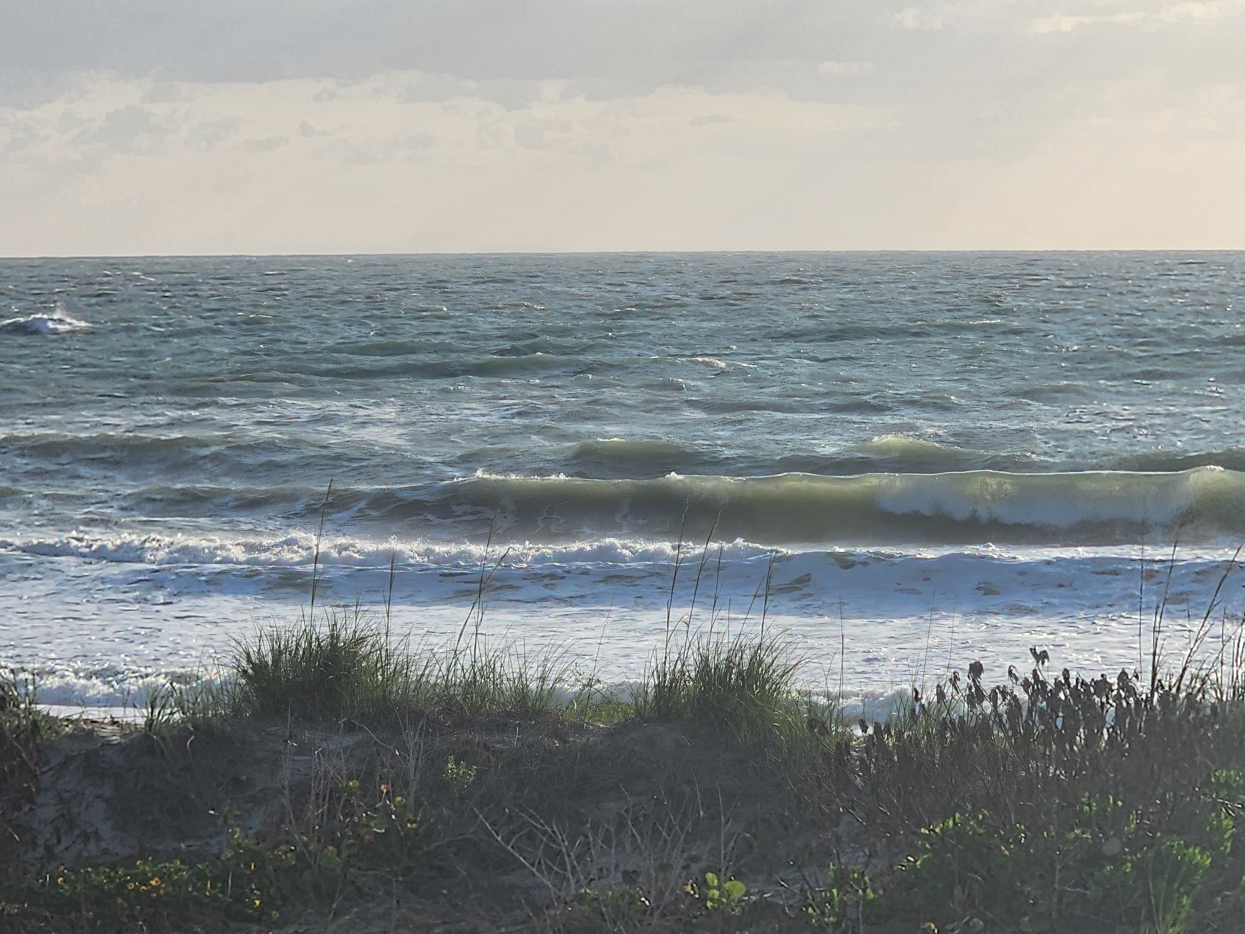 Wind-chopped 2-3 foot waves breaking through dune vegetation at Picnic Tables South Cocoa Beach overcast morning