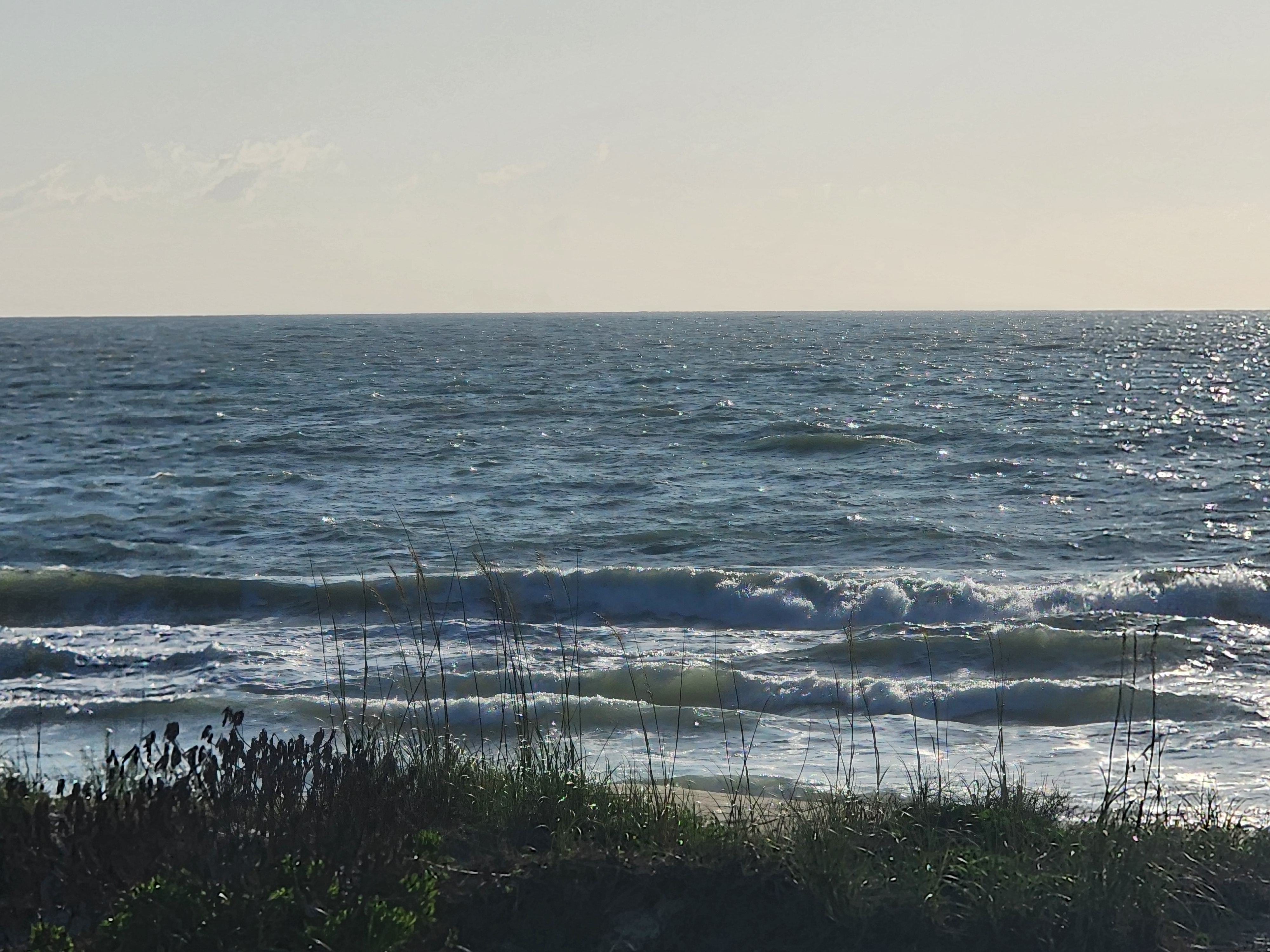 Sun sparkling off choppy surf with multiple waves breaking through sea oats at 31st Street Cocoa Beach