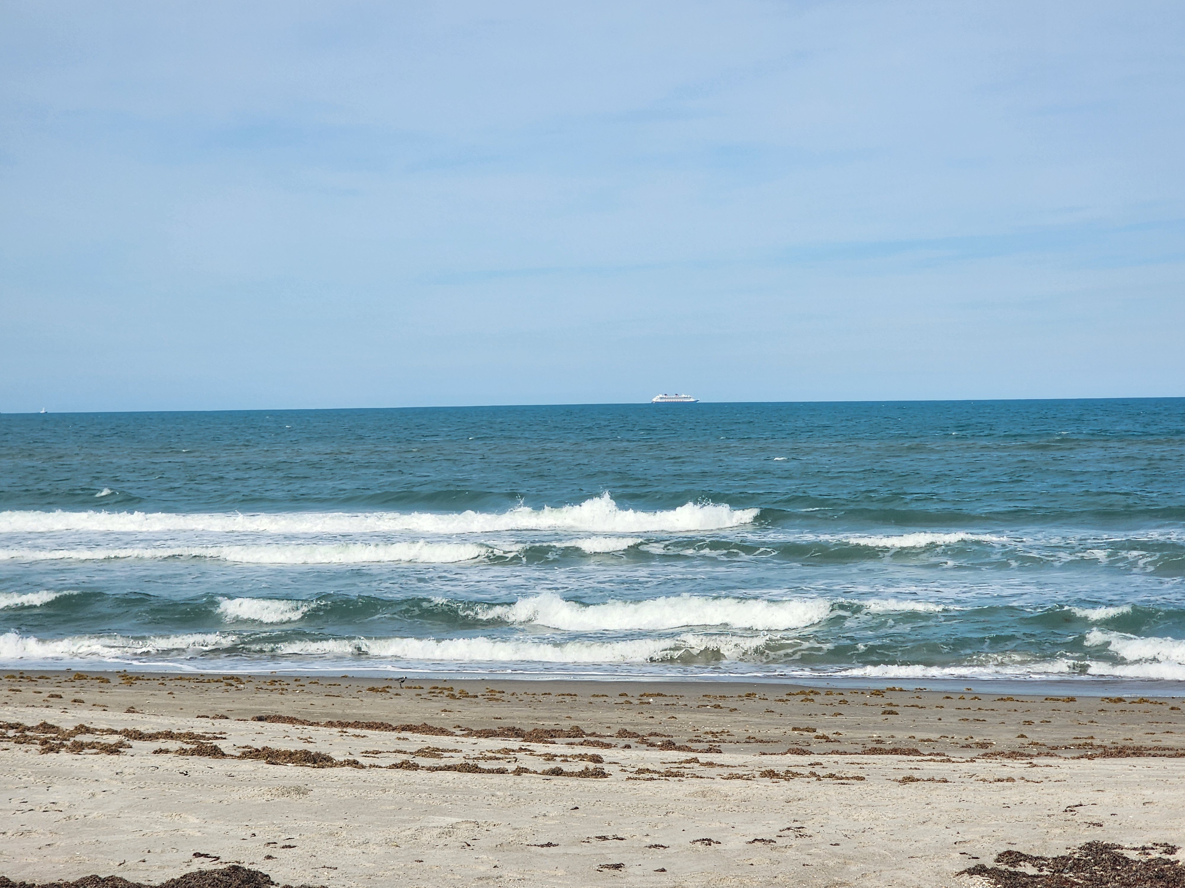 Small aquamarine waves breaking at Picnic Tables South Cocoa Beach with cruise ship passing Port Canaveral