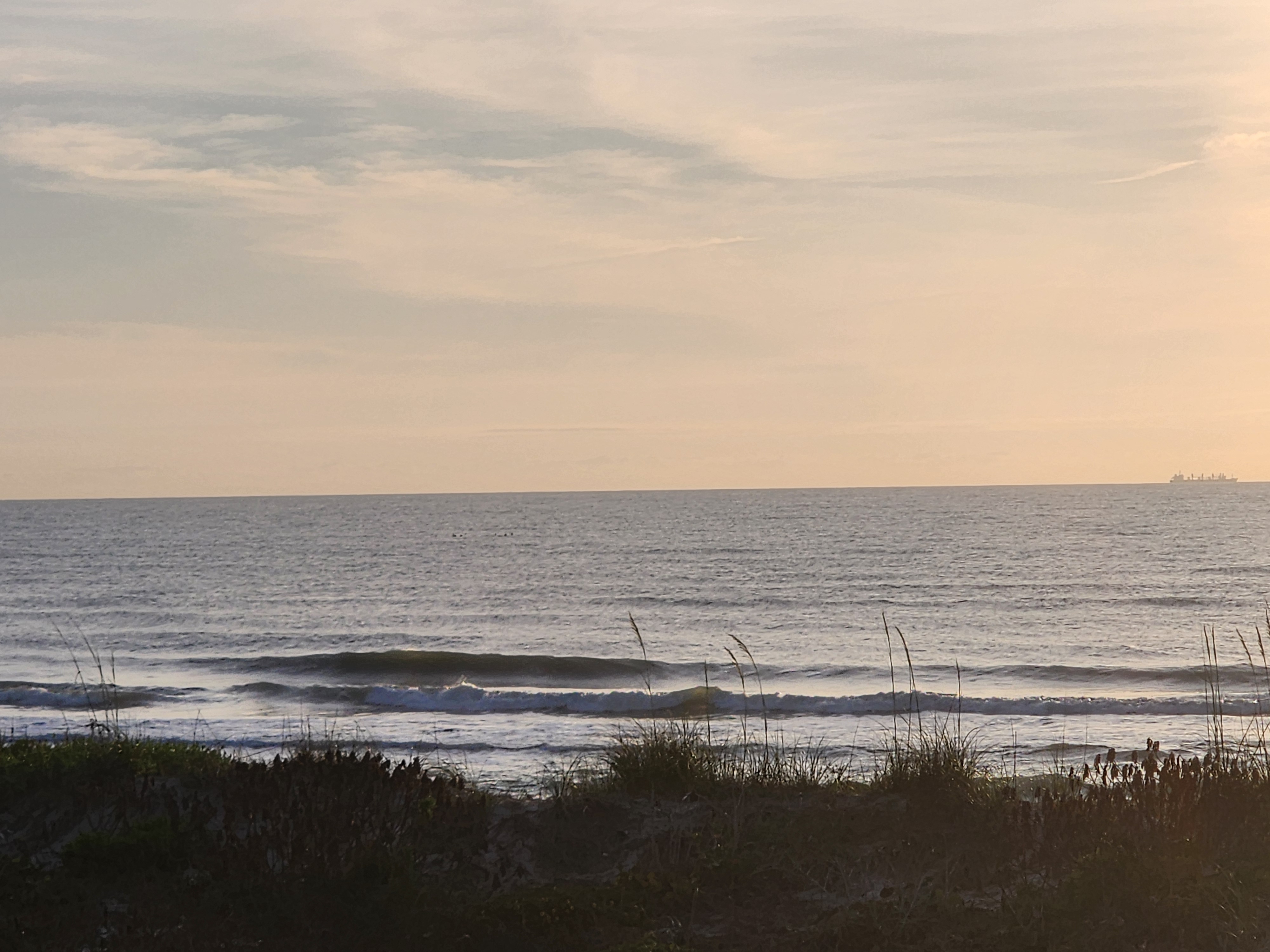 Clean 1-2 foot waves with surfers in the lineup at Picnic Tables South Cocoa Beach cargo ship on horizon