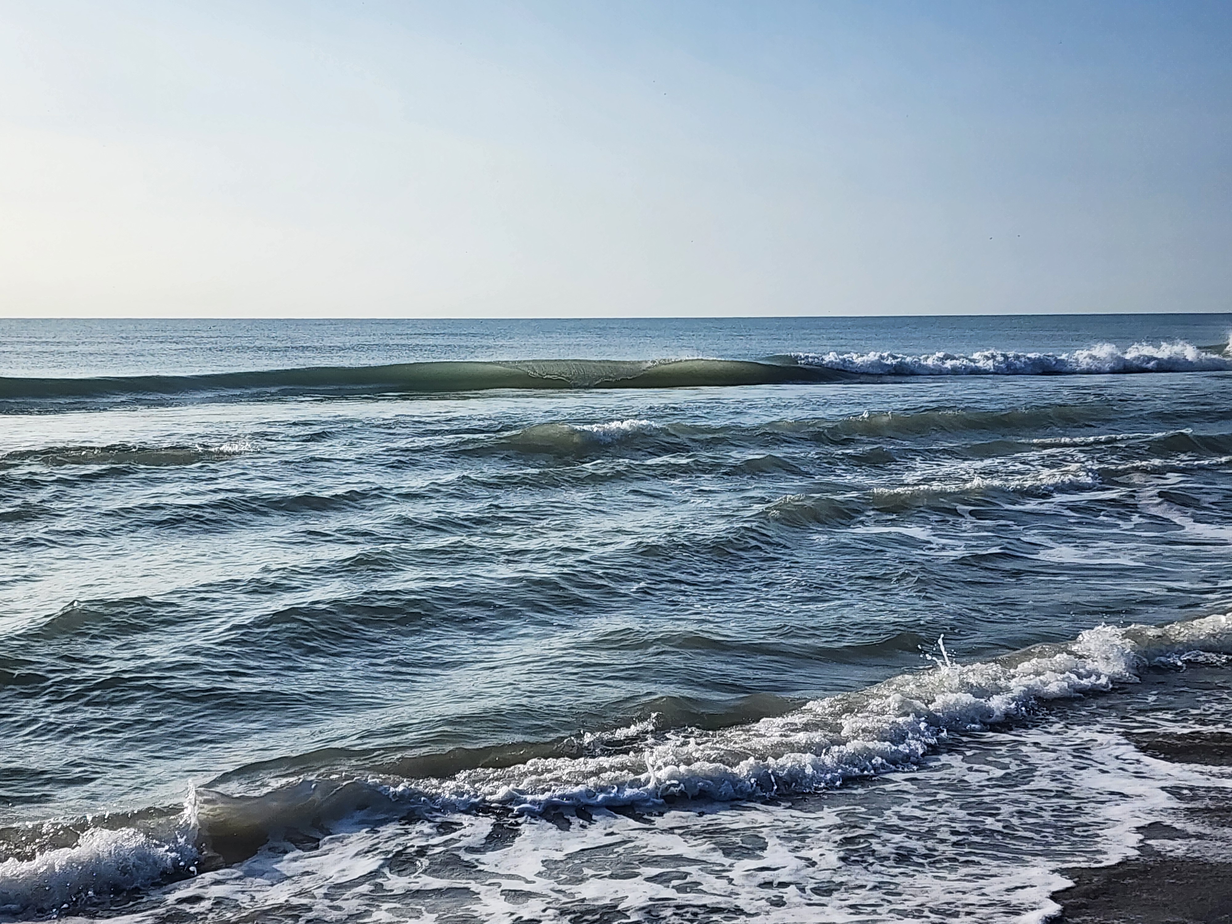 Clean glassy 1 foot wave with green face about to break on the shoreline under clear blue sky at Picnic Tables South Cocoa Beach
