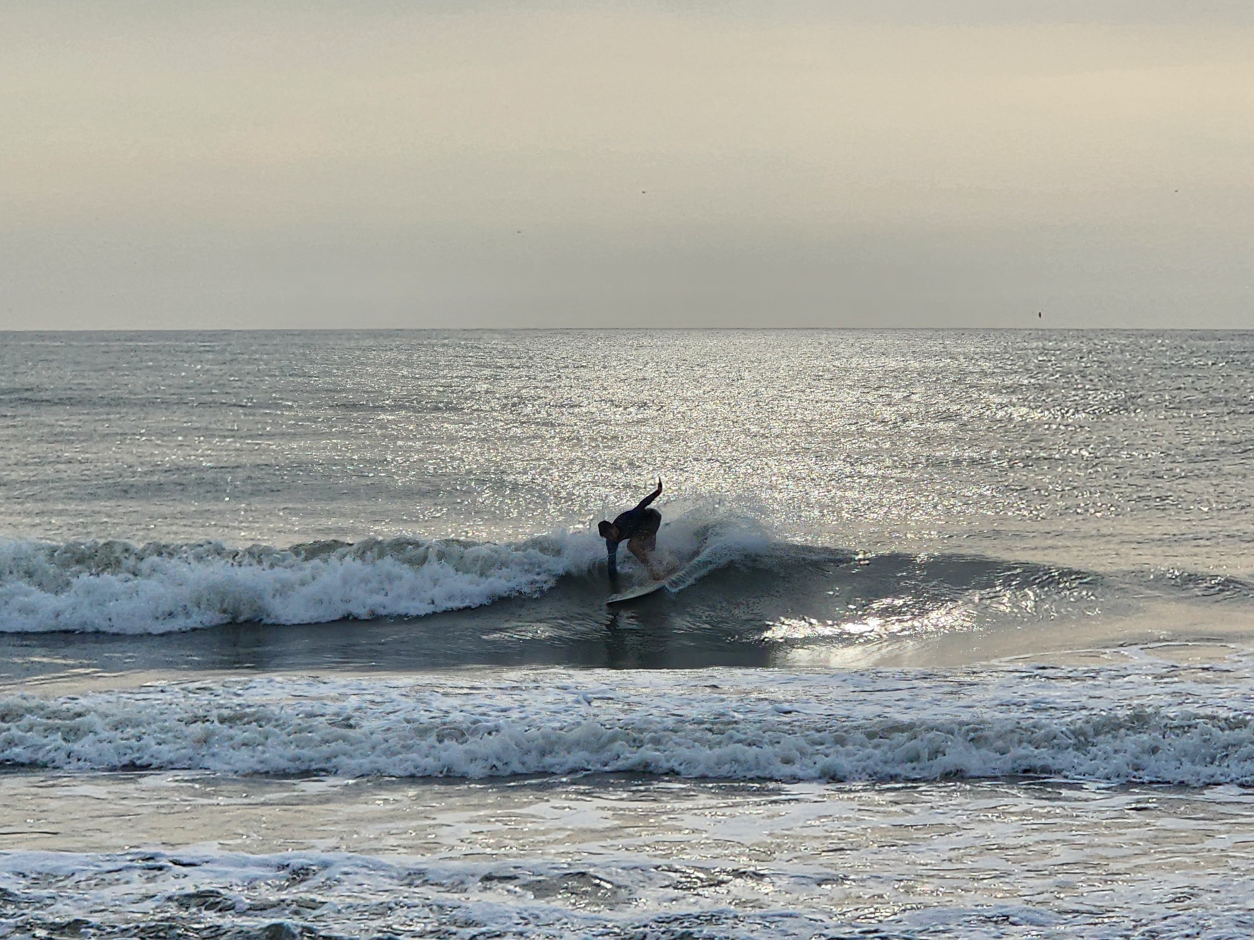 Surfer bottom turning on a backlit clean wave at lowtide sandbars Picnic Tables South Cocoa Beach Sunday morning