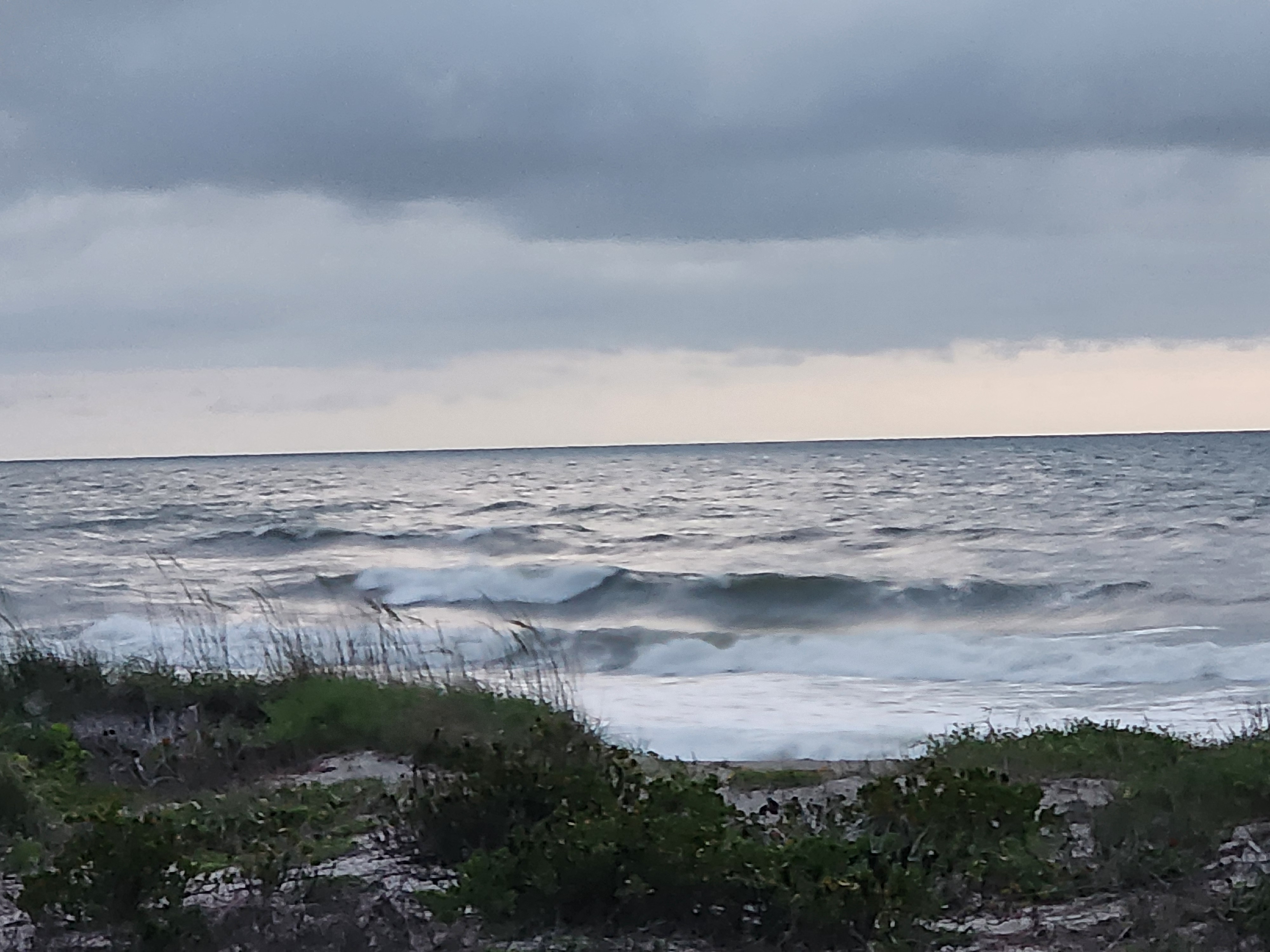 Powerful 3-4 foot windswell wave with spray breaking through dune vegetation at Picnic Tables South Cocoa Beach SE winds May 13 2026