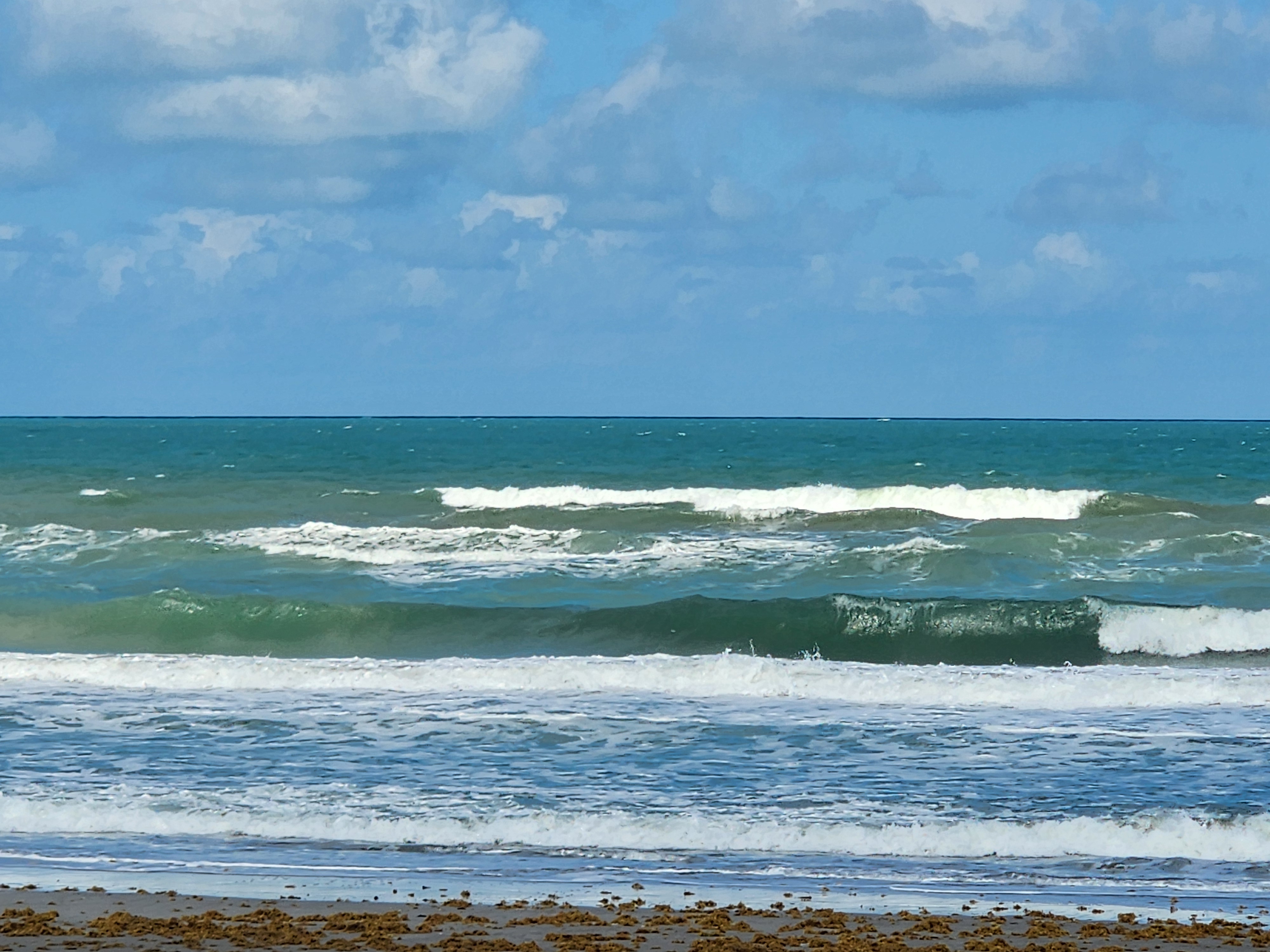 Wind textured 3 foot plus choppy wave lines breaking under blue sky with scattered clouds at low tide in South Cocoa Beach Tuesday afternoon