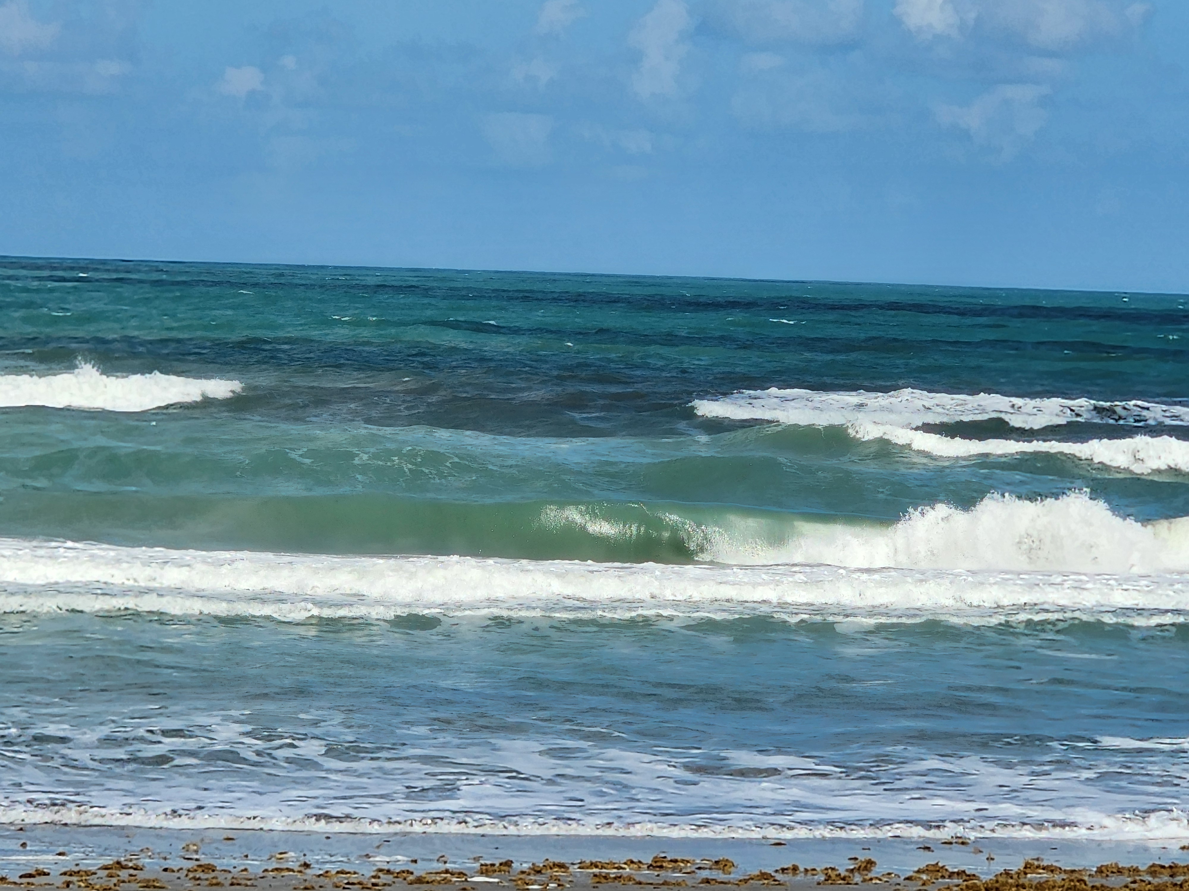 Close view of a green choppy wave breaking nearshore with ESE wind texture and whitewater at Picnic Tables South Cocoa Beach low tide