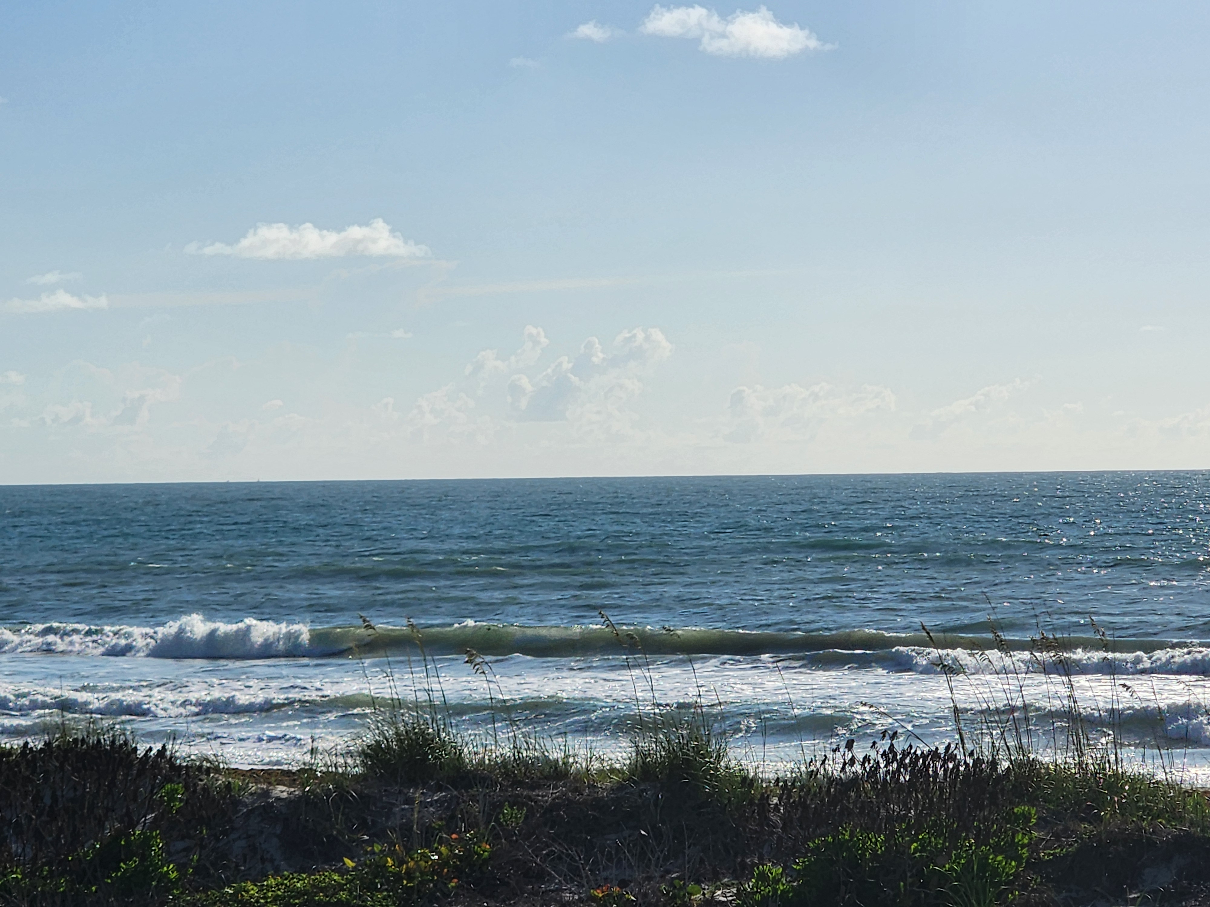Waist high waves breaking at Picnic Tables in South Cocoa Beach with sea oats in the foreground and morning sunlight sparkling on the water