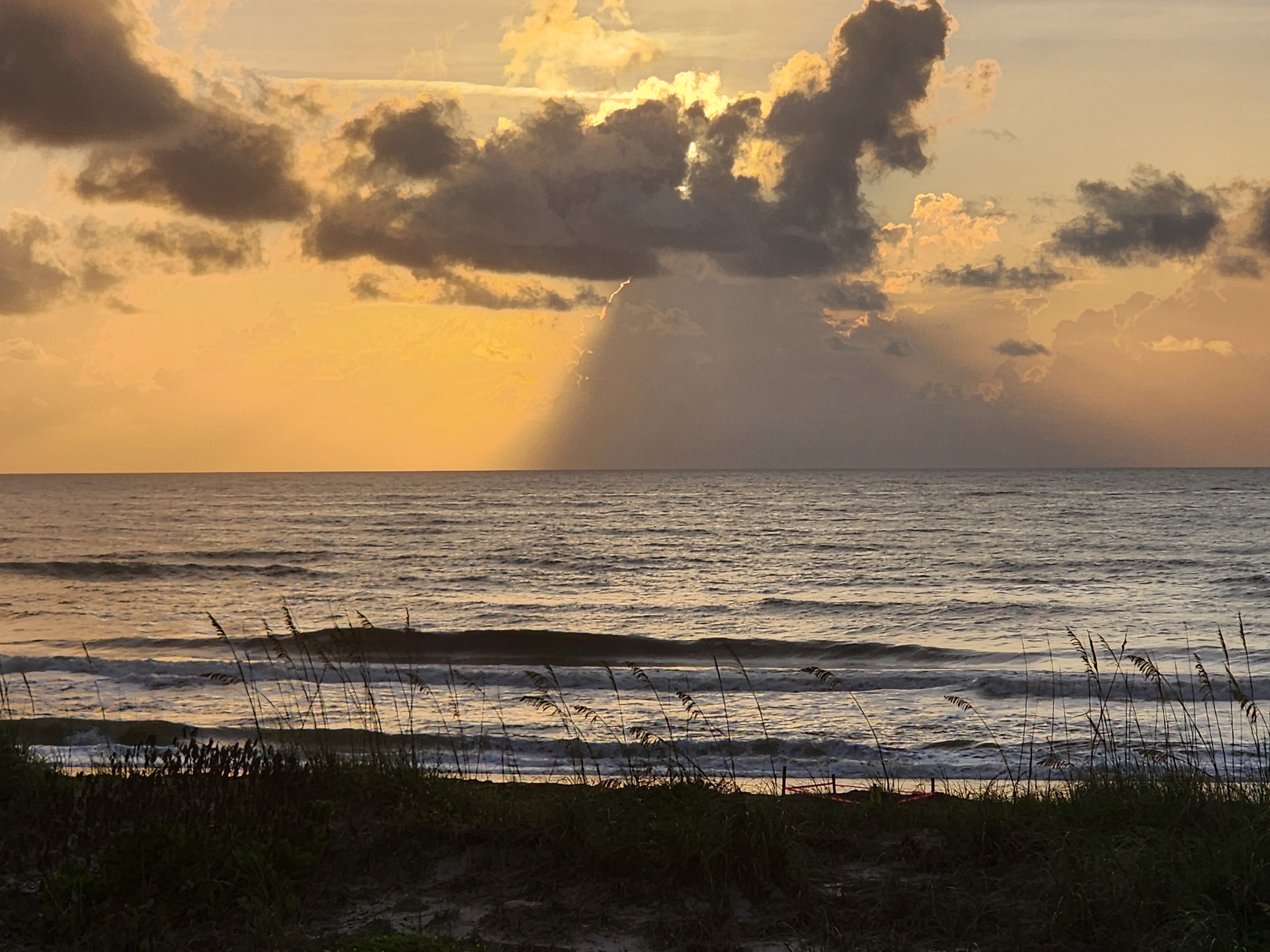 Sun rays streaming through towering cumulus clouds over rolling waves at Picnic Tables Cocoa Beach