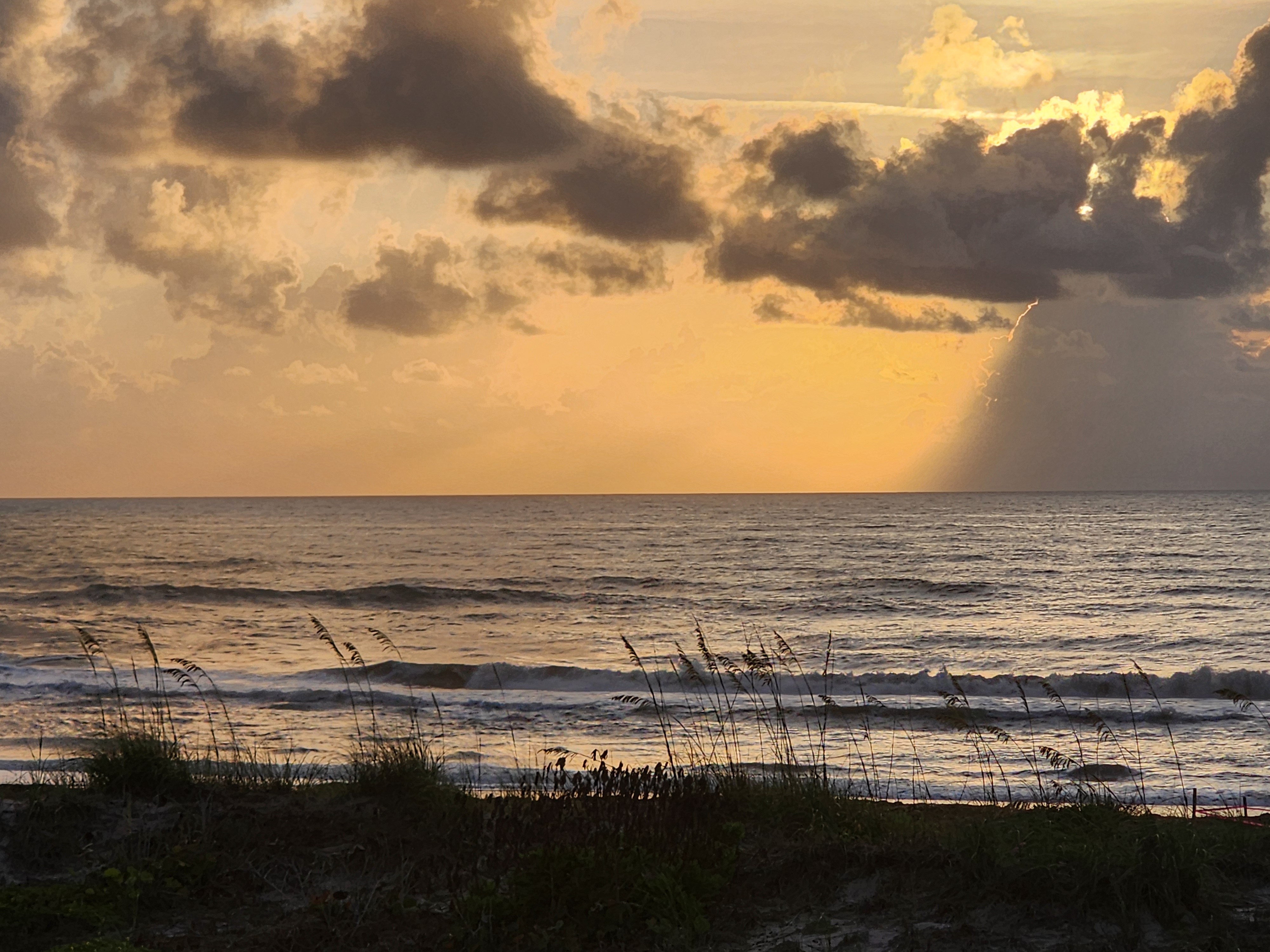 Dramatic cloud formations with golden light and sea oats silhouetted against morning surf South Cocoa Beach