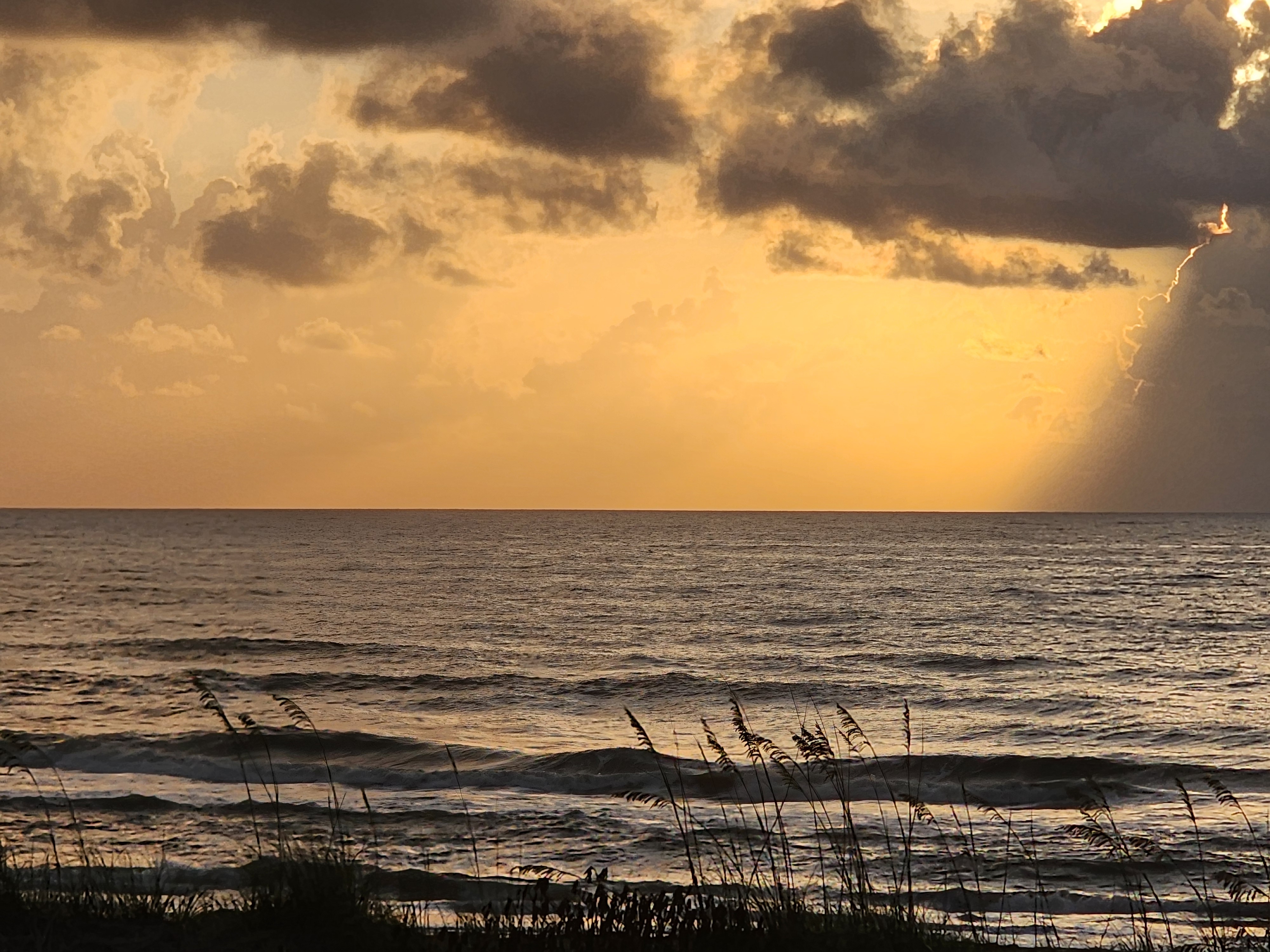 Dark moody sunrise with golden glow reflecting off choppy surf and sea oats at South Cocoa Beach