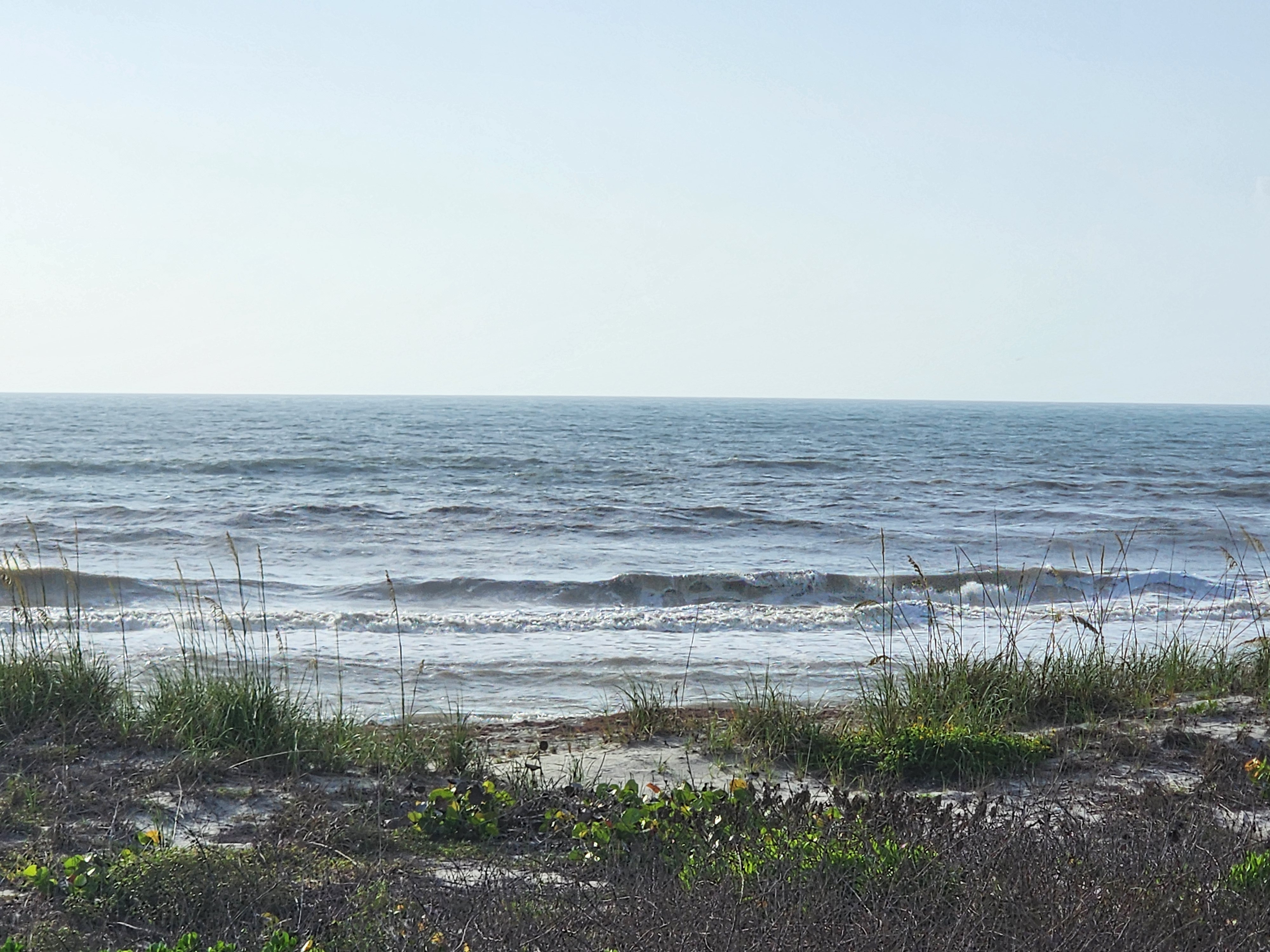 Hazy morning view of small choppy waves breaking through sea oats and dune vegetation at Picnic Tables South Cocoa Beach