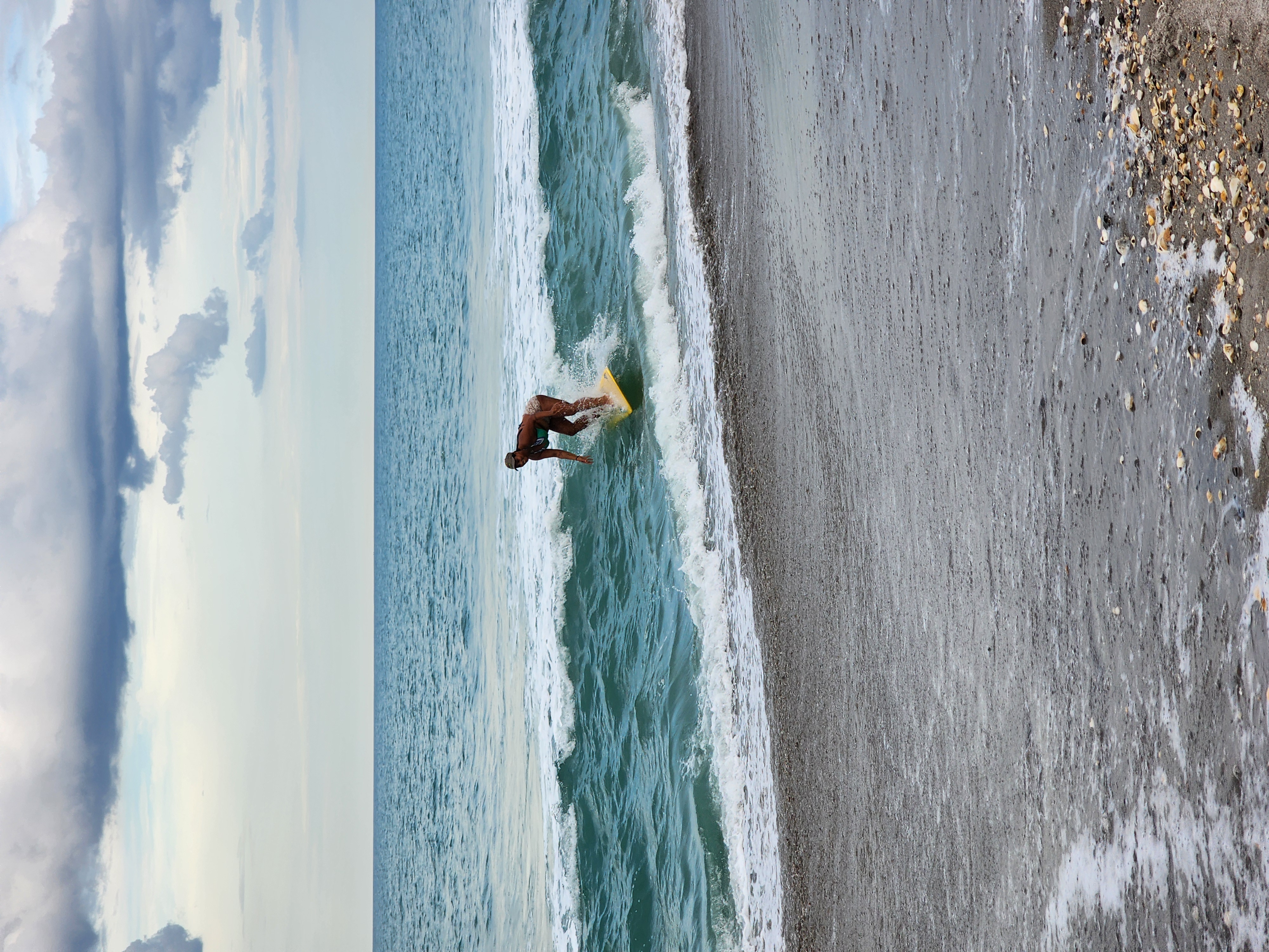 Surfer dropping into a 1 foot wave on yellow longboard with cloudy skies at South Cocoa Beach evening session