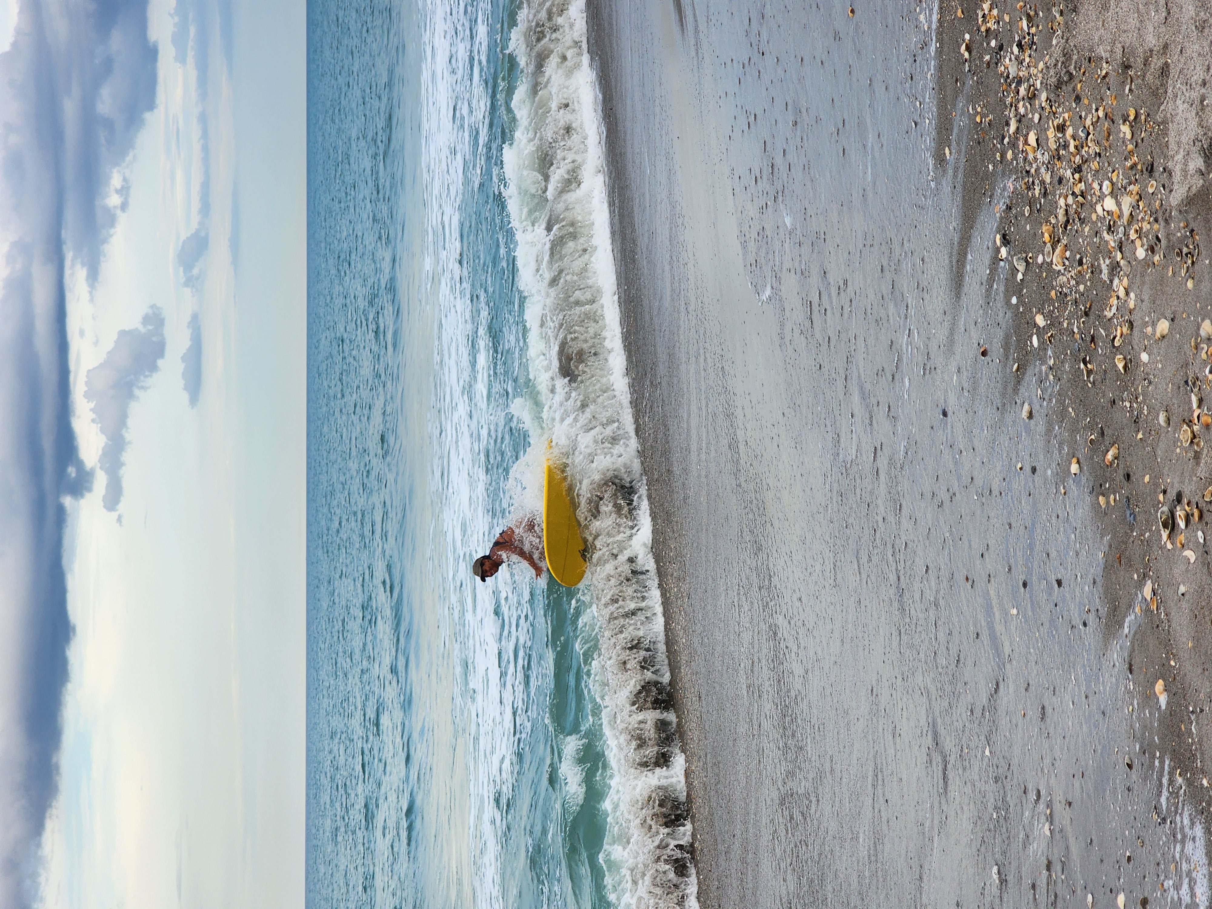Surfer pushing through shorebreak with yellow longboard in crystal clear water at Cocoa Beach best surf spot