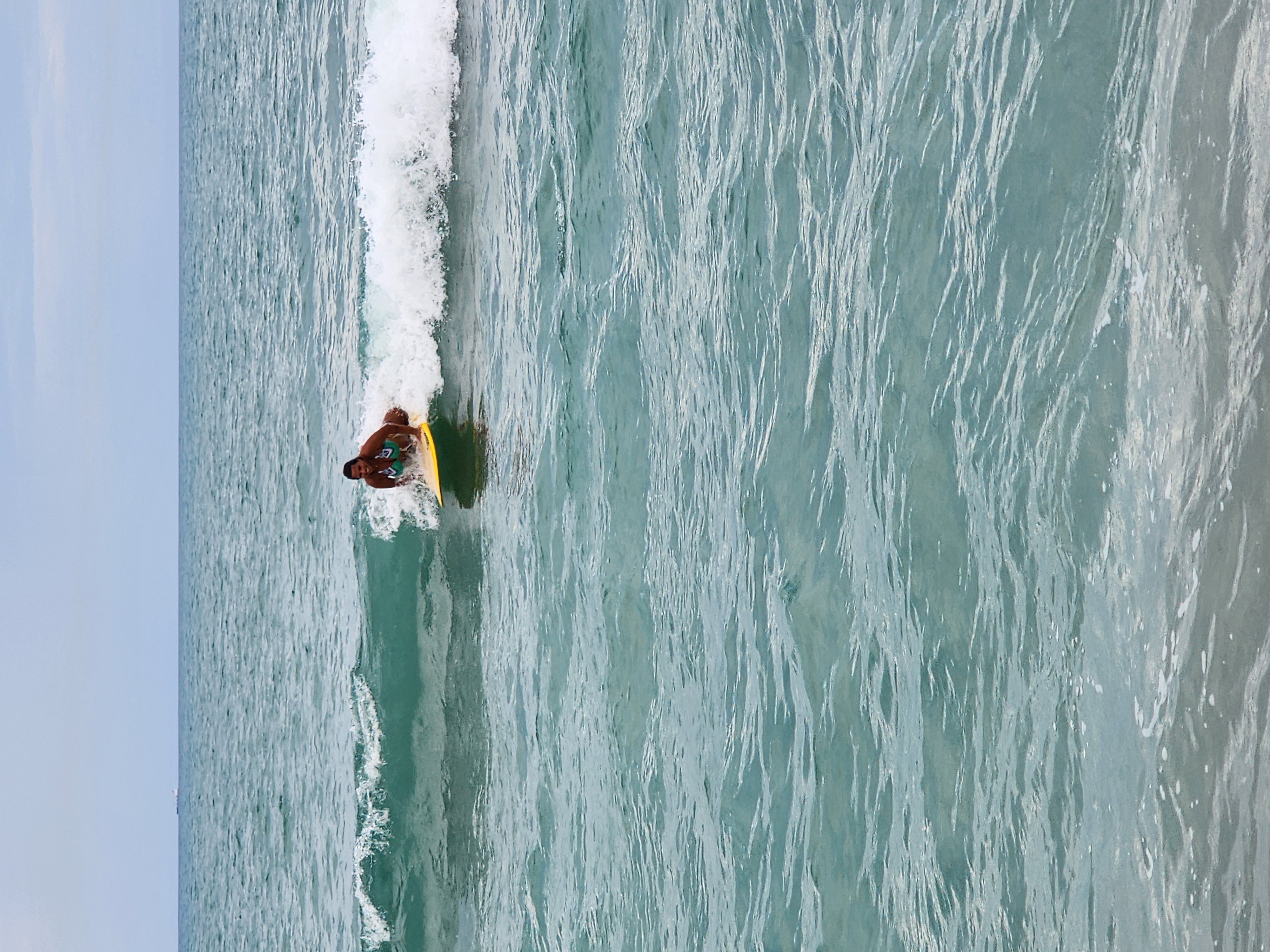 Longboarder catching a small clean wave in emerald green water at South Cocoa Beach evening training session