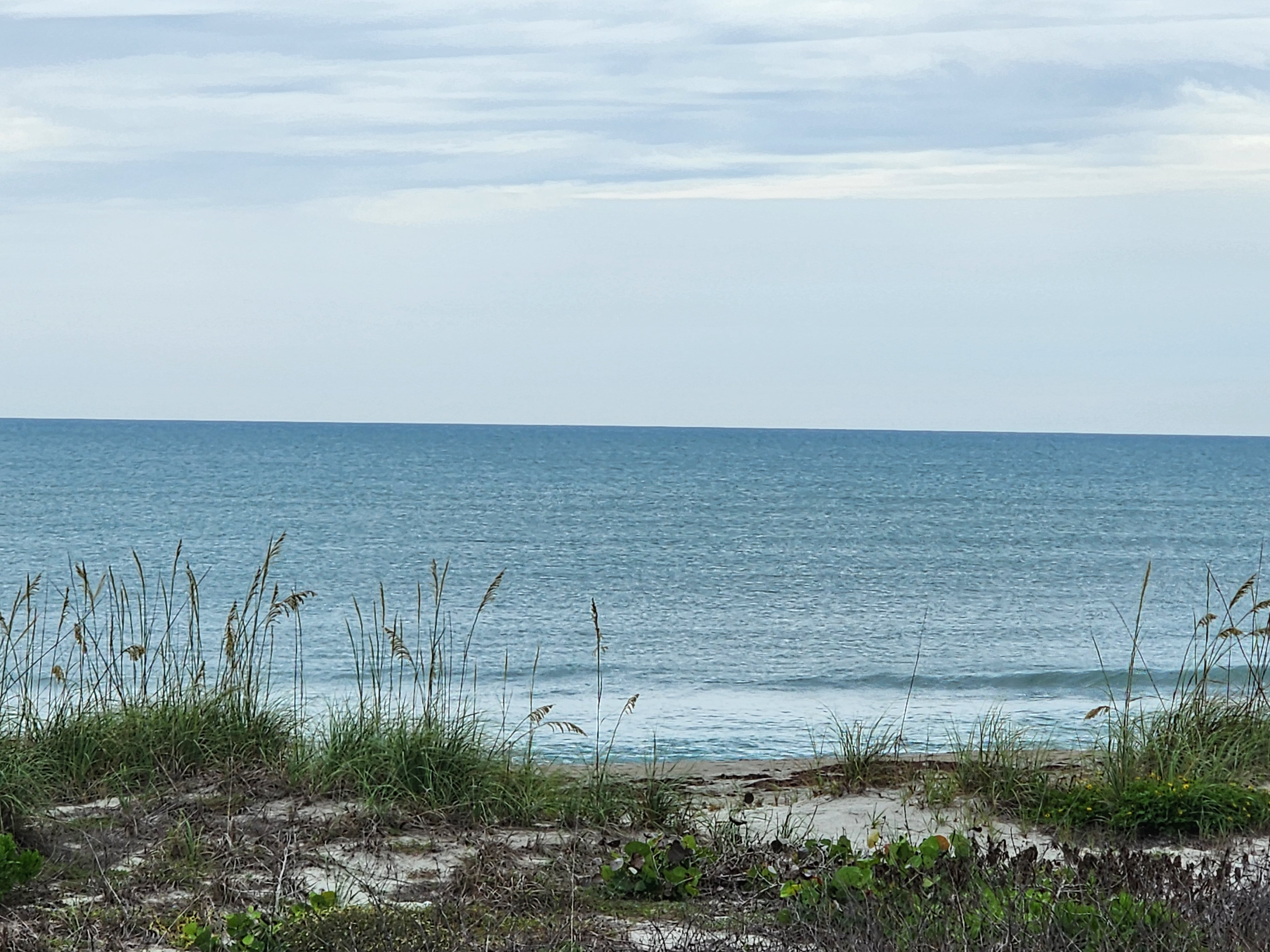 Nearly flat 1 foot surf with aquamarine water and sea oats at Picnic Tables South Cocoa Beach