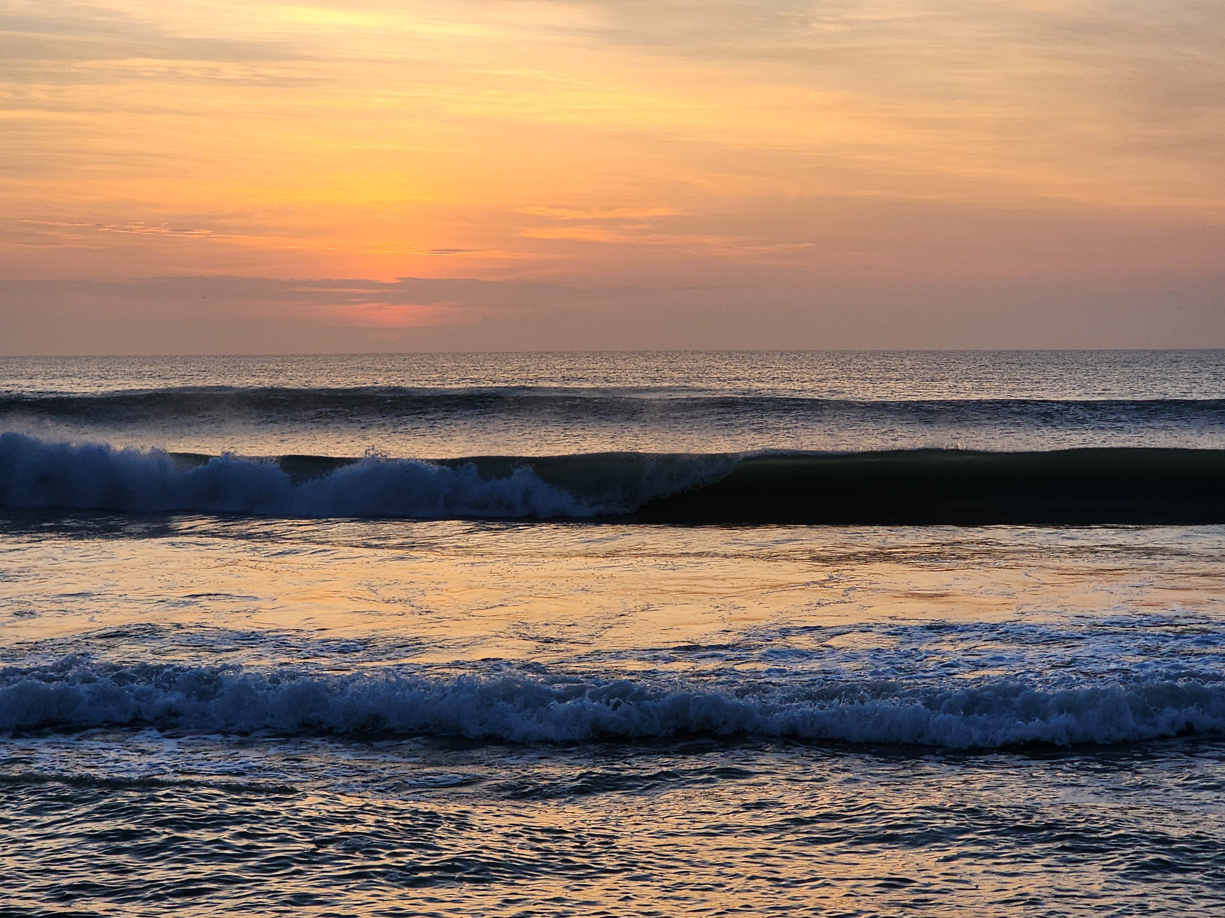 Thick hollow wave breaking with golden orange sunrise reflected on water at Cocoa Beach NE swell surf alert