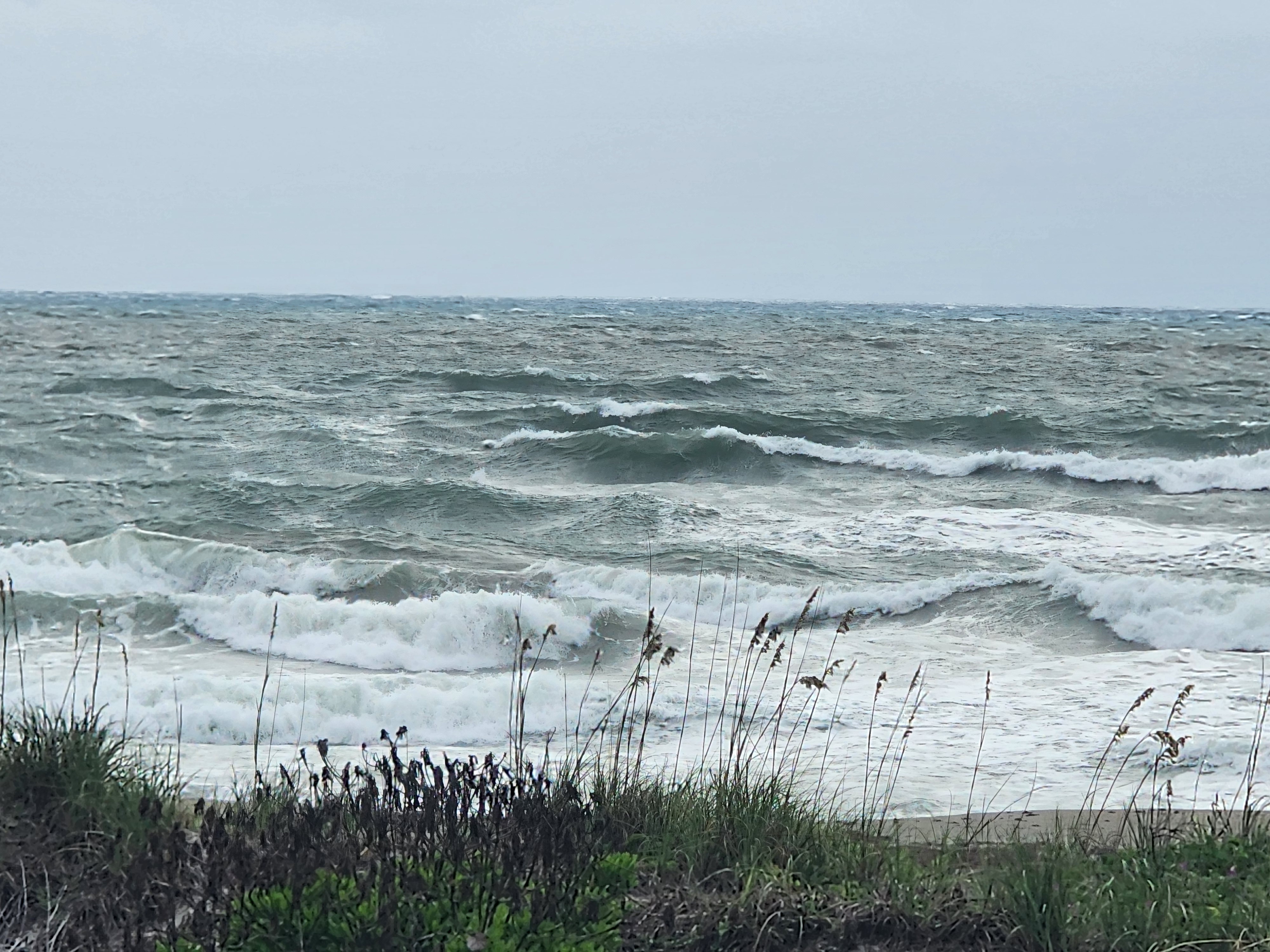 Wide view of blown-out surf with multiple lines of whitecap waves under grey overcast skies at Picnic Tables Cocoa Beach