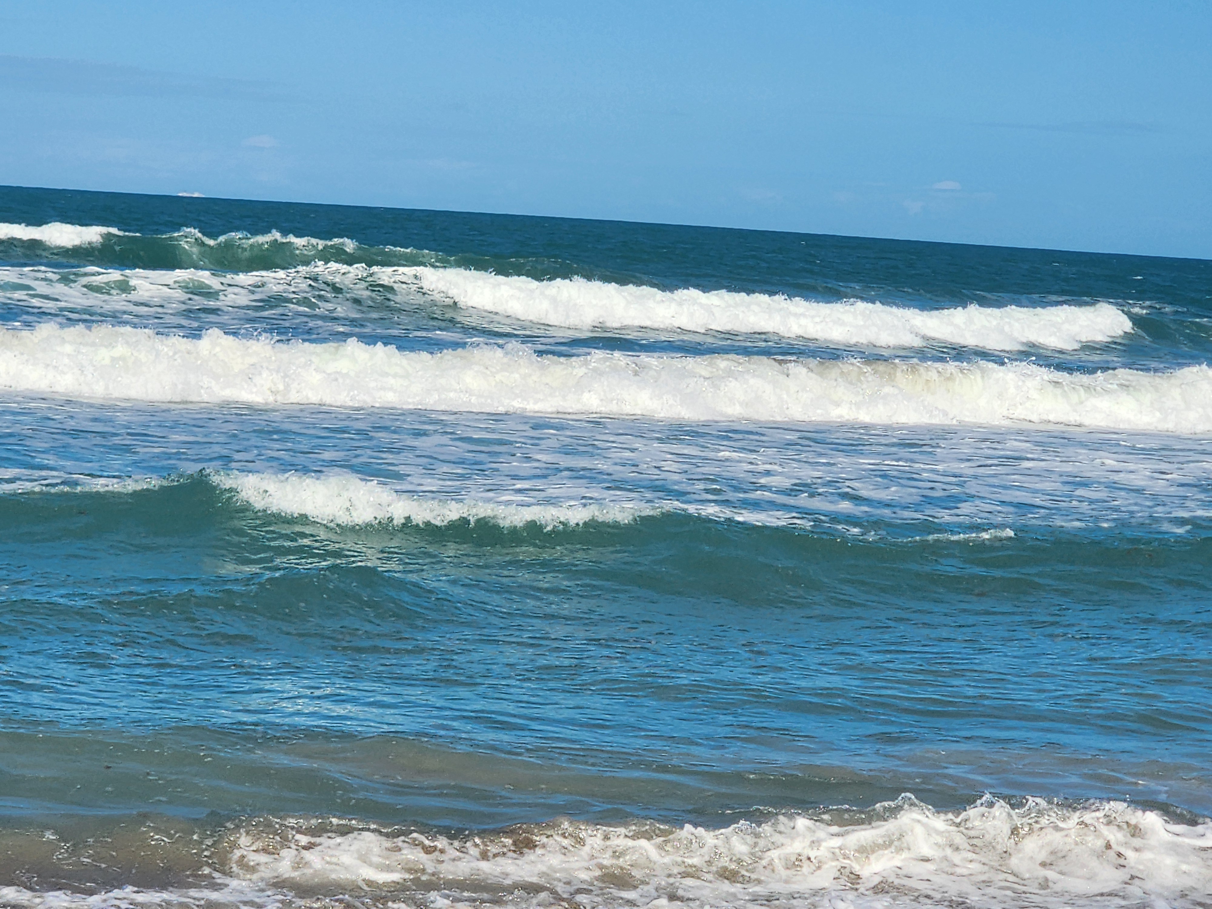 Clean blue water with 3-4 foot swell lines and light onshore texture at Picnic Tables Cocoa Beach lowtide