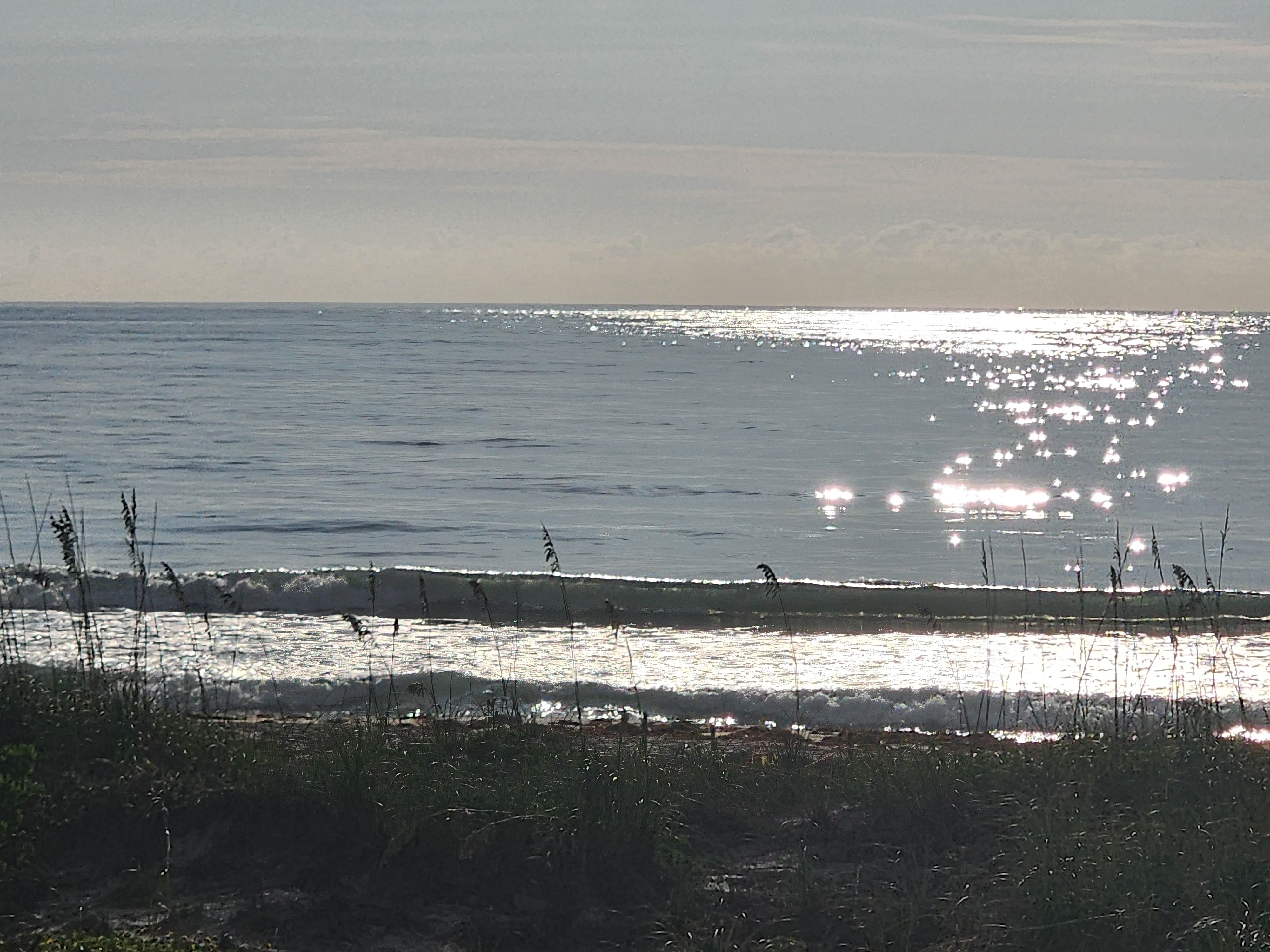 Morning sun glittering on a glassy ocean with a small clean wave breaking near shore at Picnic Tables, South Cocoa Beach, June 2026
