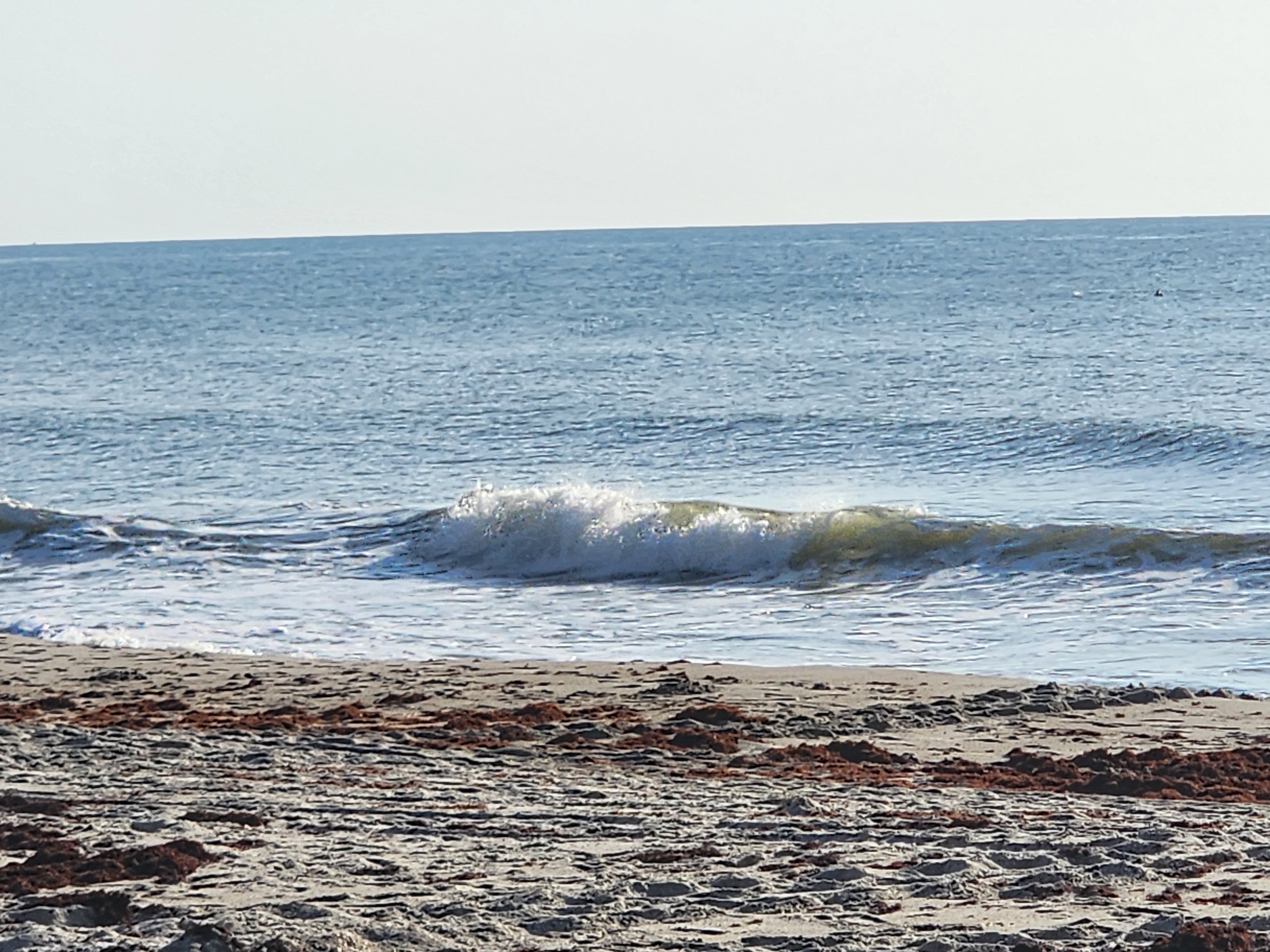 Tiny waist-high-at-best wave folding over close to the sand under a hazy bright sky