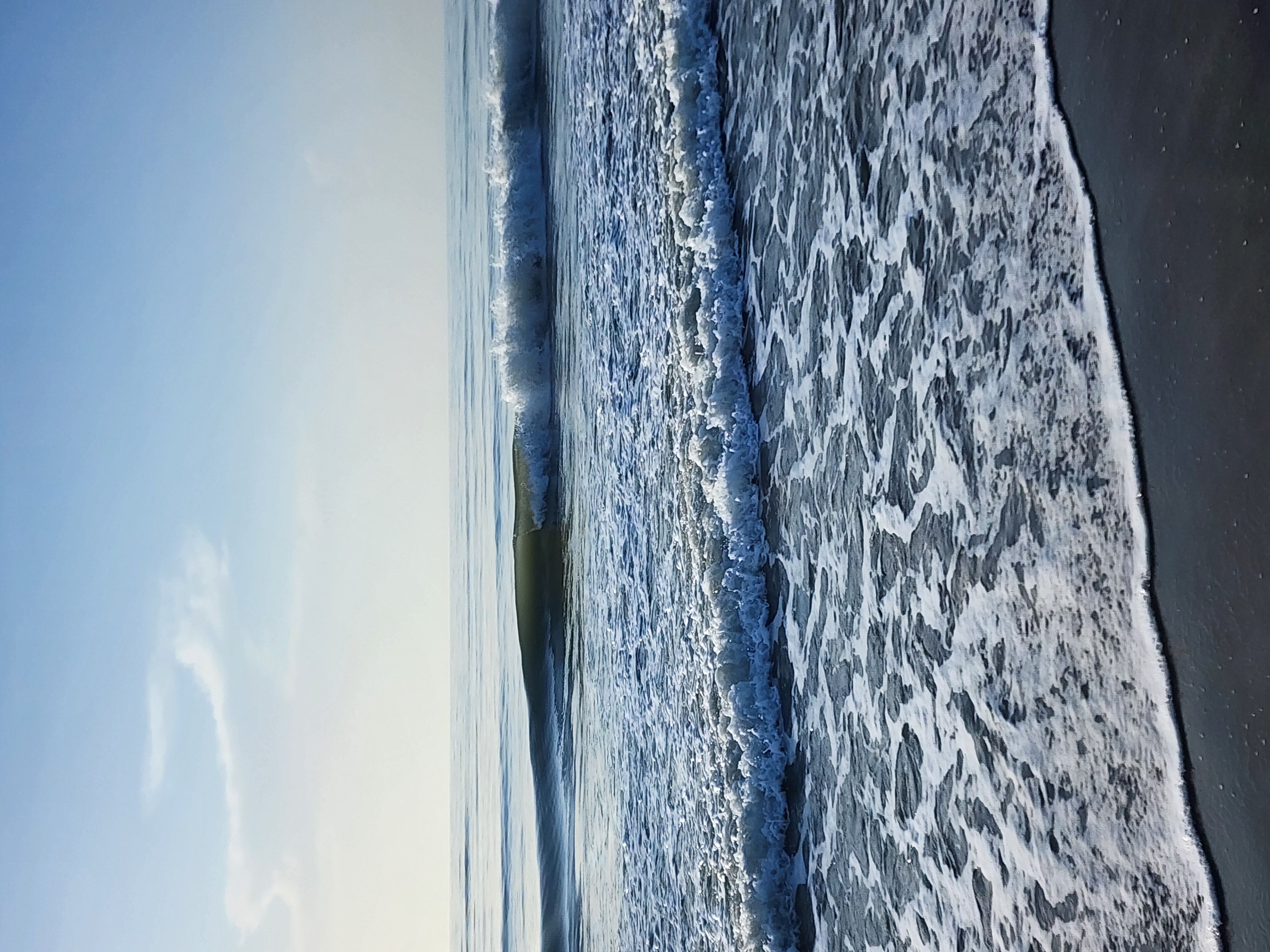 Close-up of a clean little wave breaking nearshore at the shoreline, foamy whitewater washing up the wet sand.