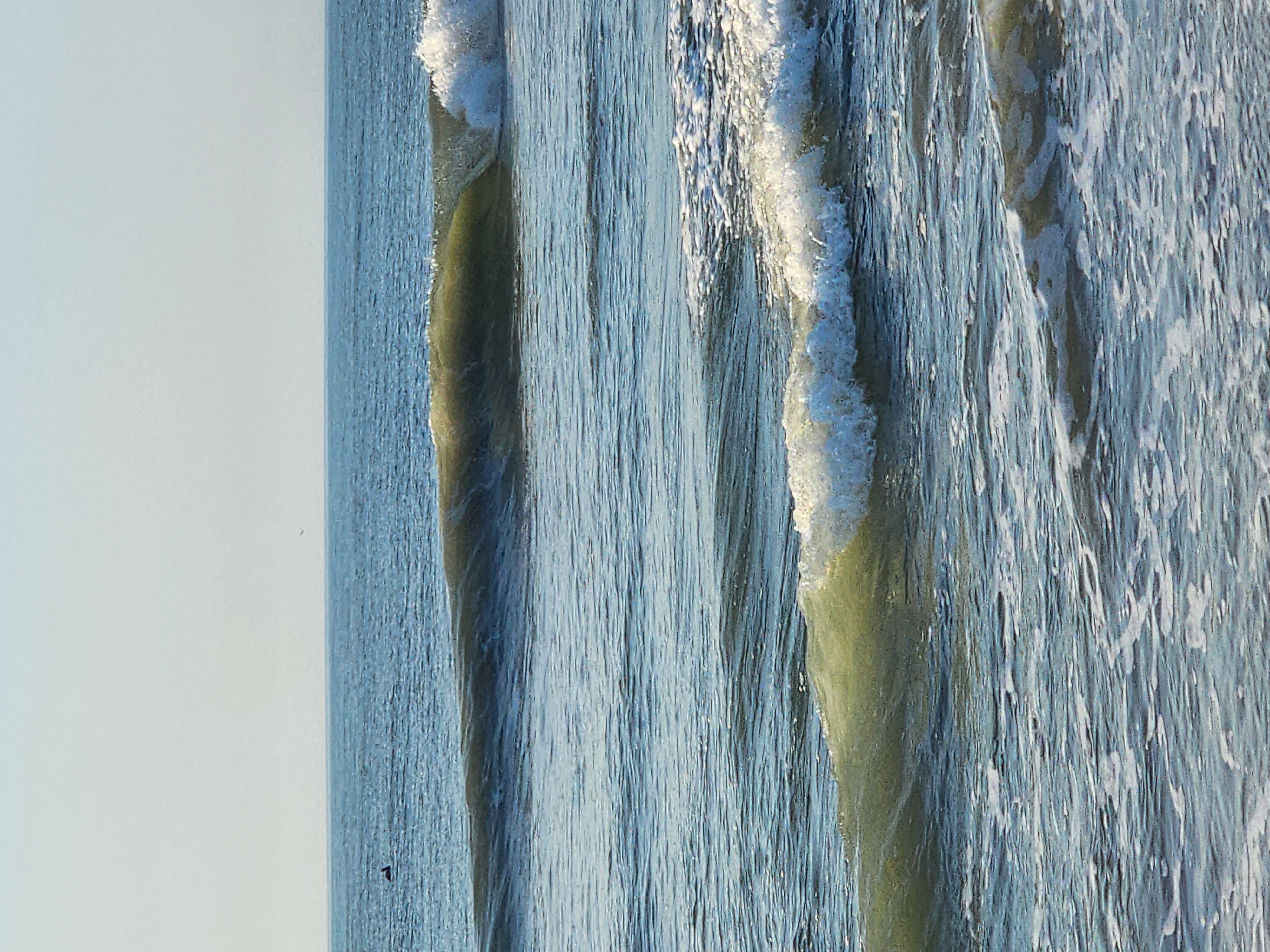 Close-up of two clean glassy waves stacking up and breaking, green-gold faces lit by the morning sun with a pelican sitting on the water in the distance.