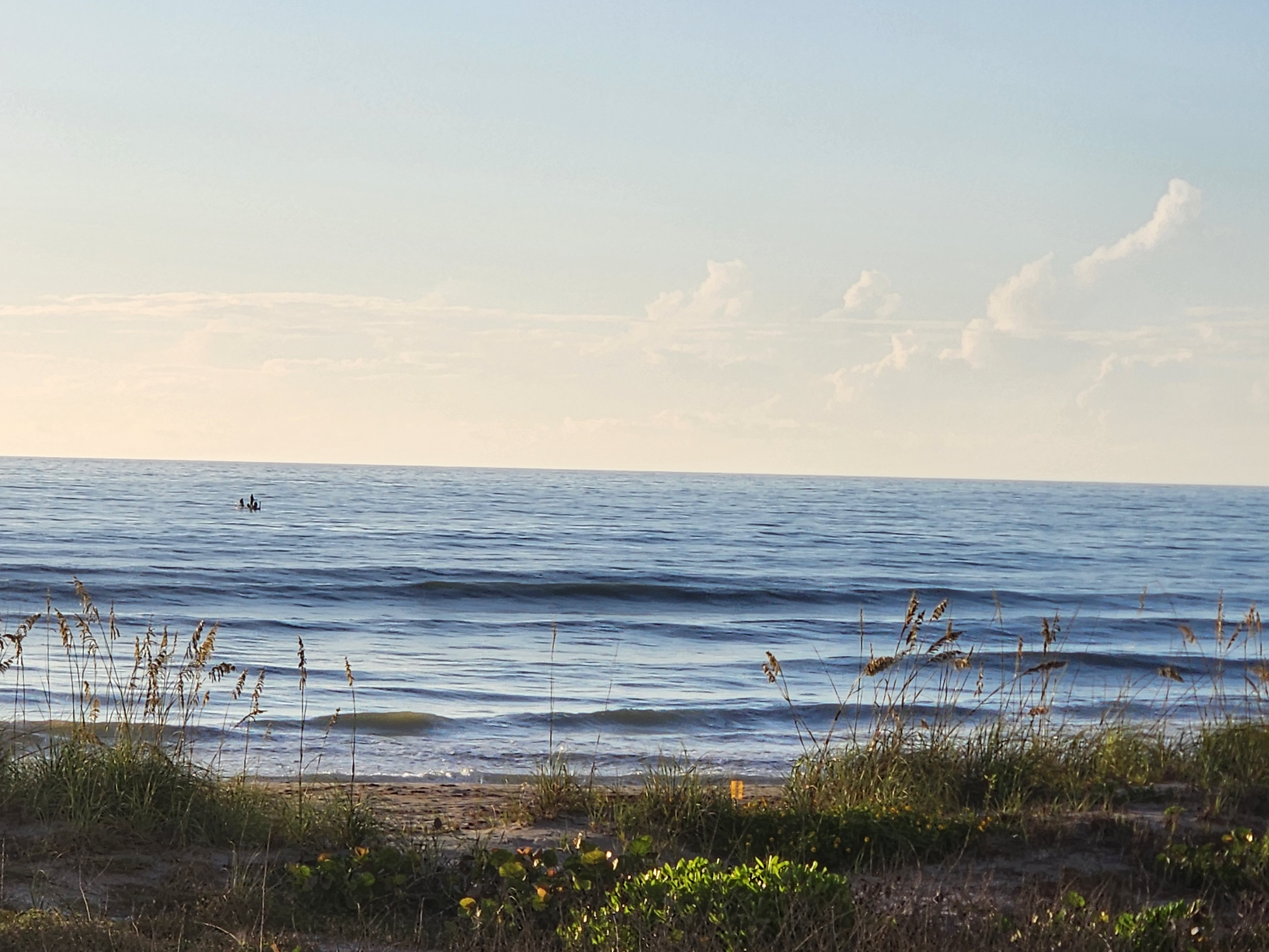 Wide view of clean groundswell lines and light offshore texture, with the anglers' skiff sitting on the horizon and puffy clouds building overhead.