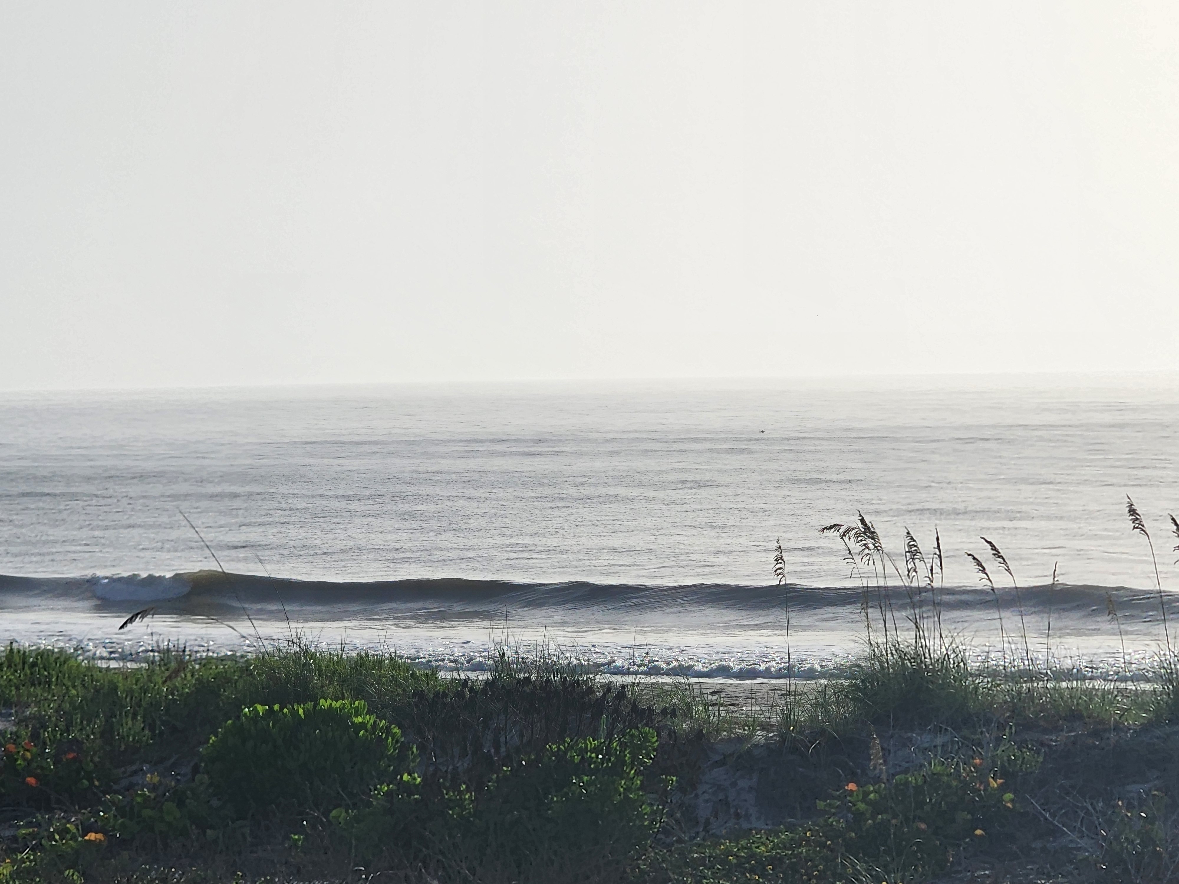Small wave peeling under hazy overcast sky at low tide, South Cocoa Beach, July 2026