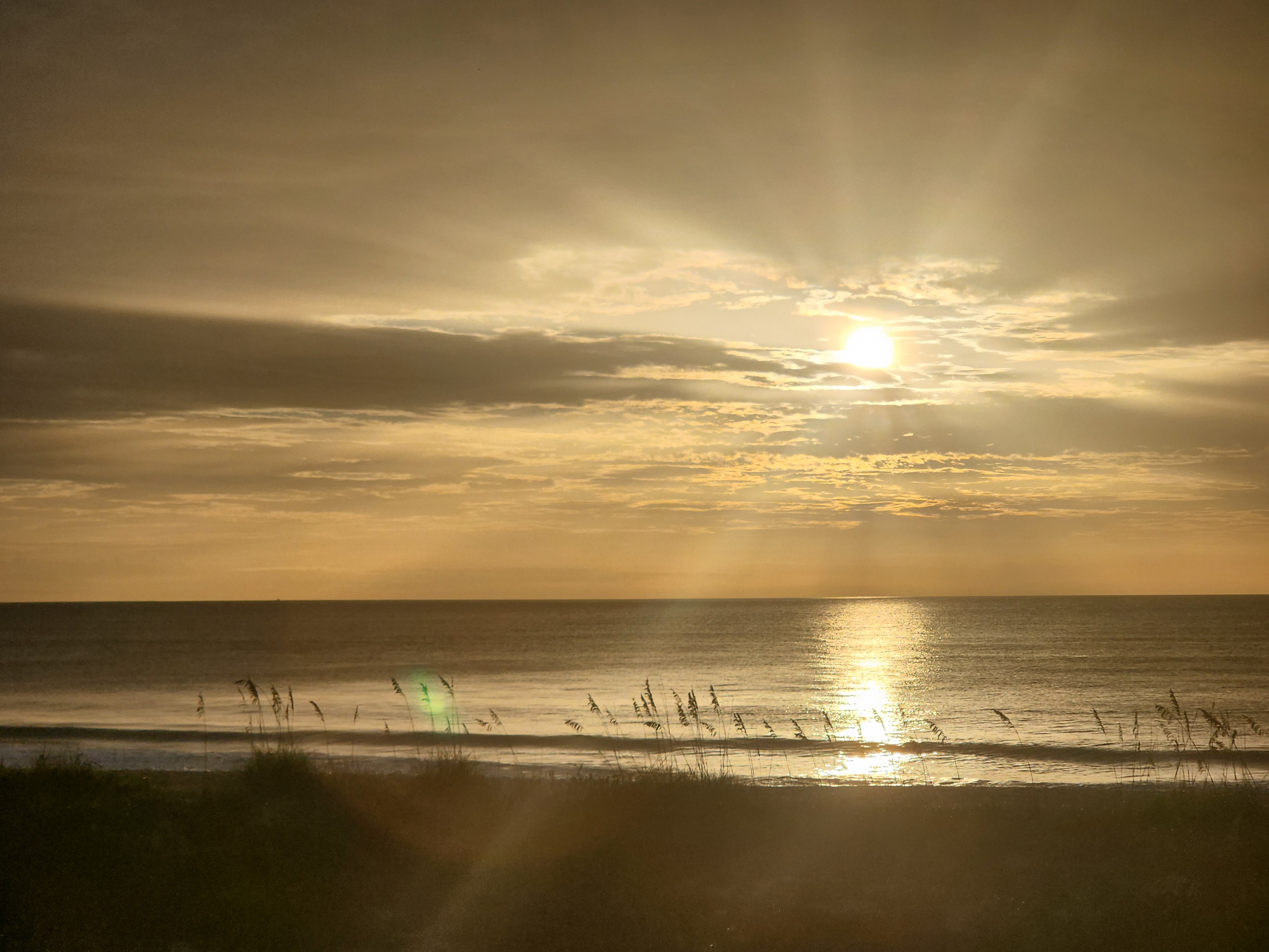 Golden sunrise light breaking through clouds over the ocean, South Cocoa Beach, July 2026