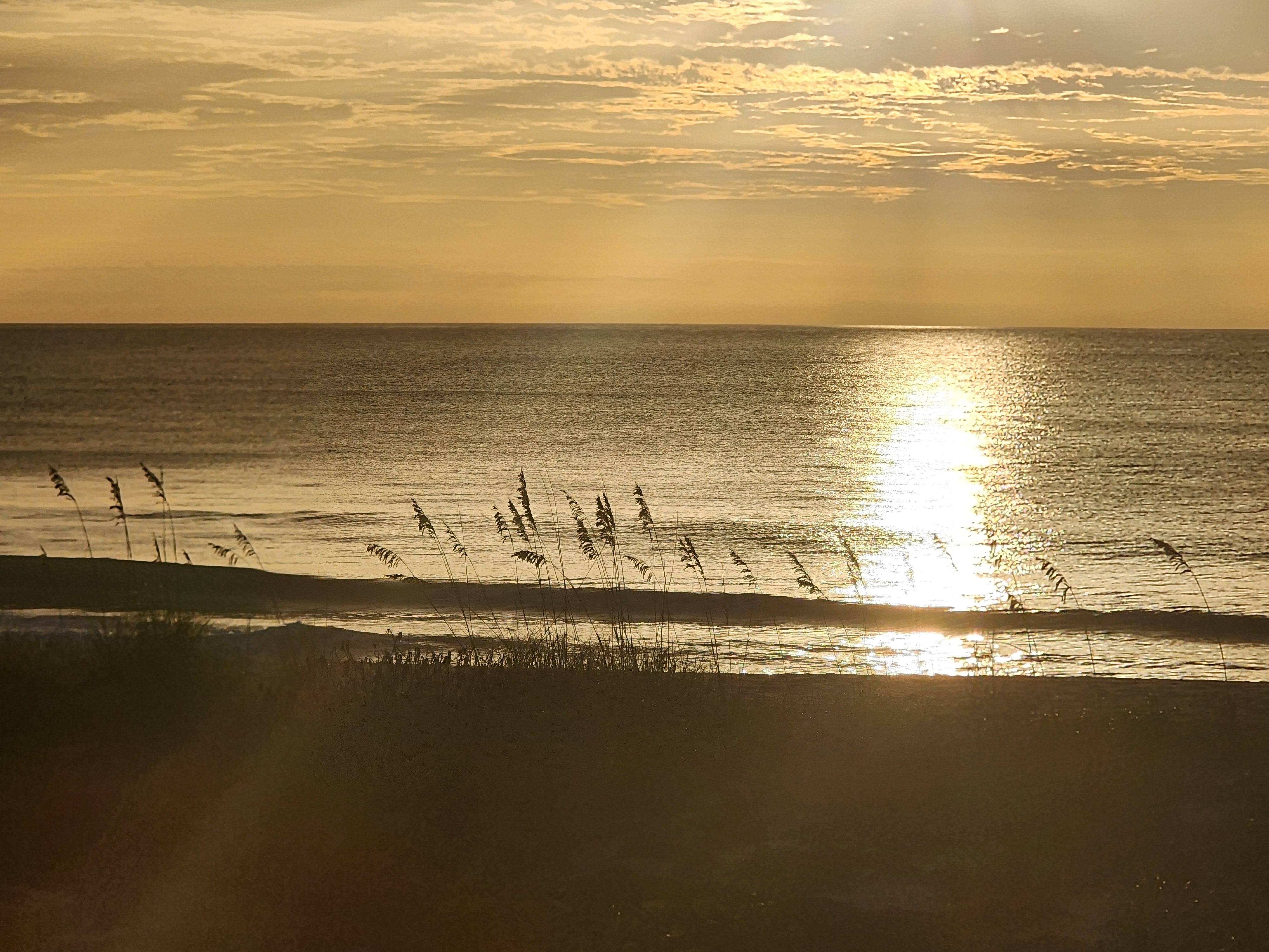Sun glow reflecting on calm water beneath a cloudy sky, South Cocoa Beach, July 2026