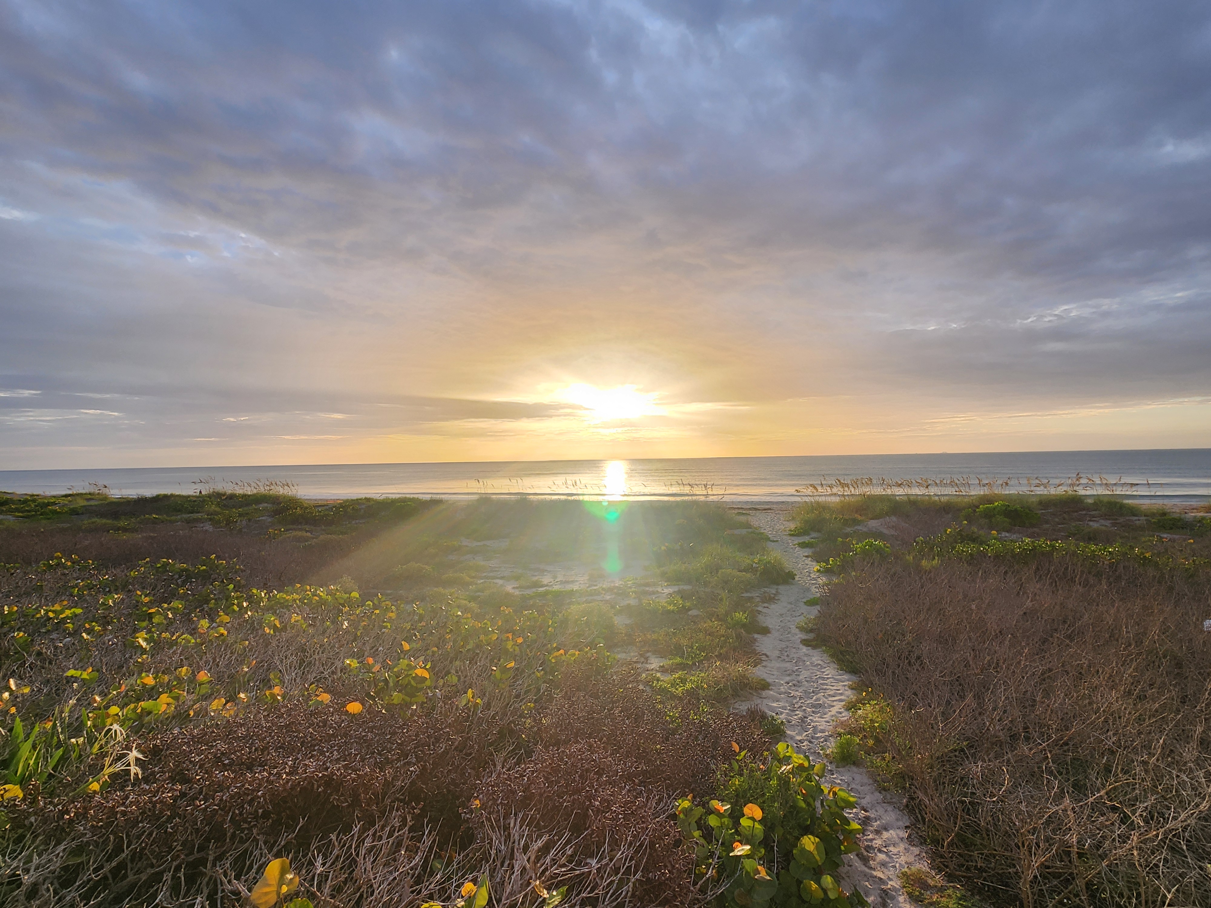 Sandy dune path leading toward a glowing sunrise over the ocean, South Cocoa Beach, July 2026