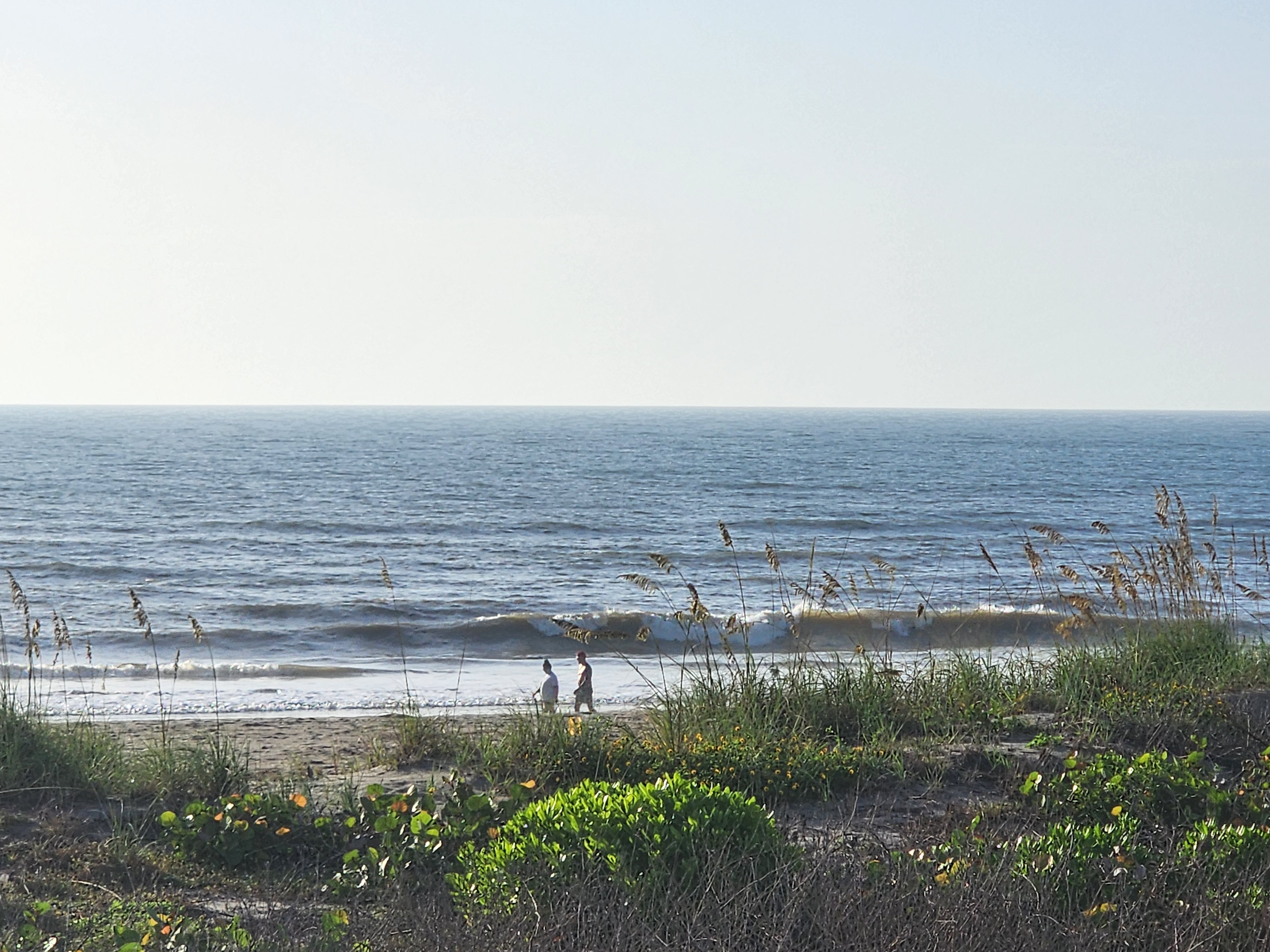Two beachgoers walking the shoreline as small waves break, South Cocoa Beach