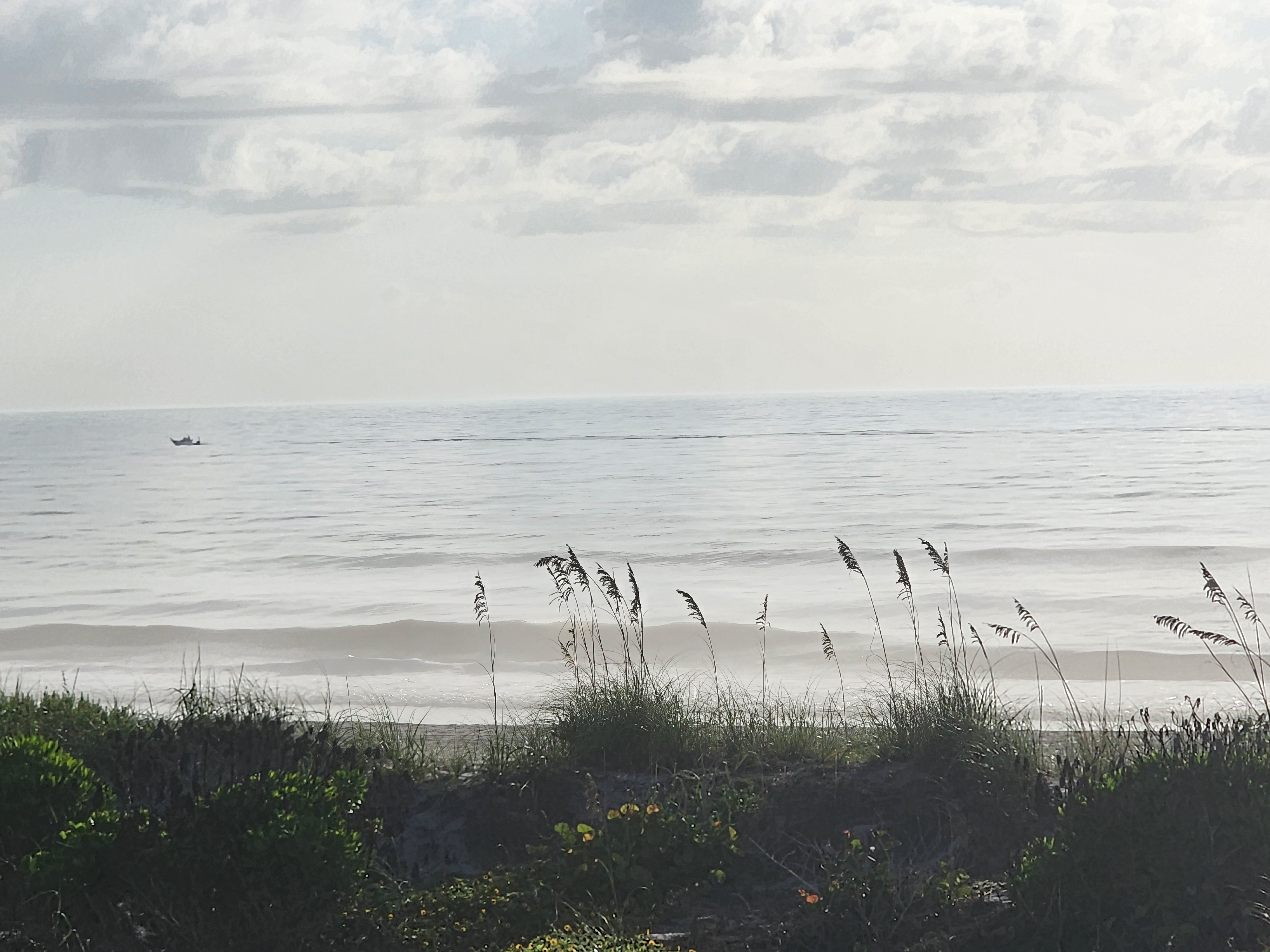 Distant boat on flat glassy water beyond the dunes, South Cocoa Beach