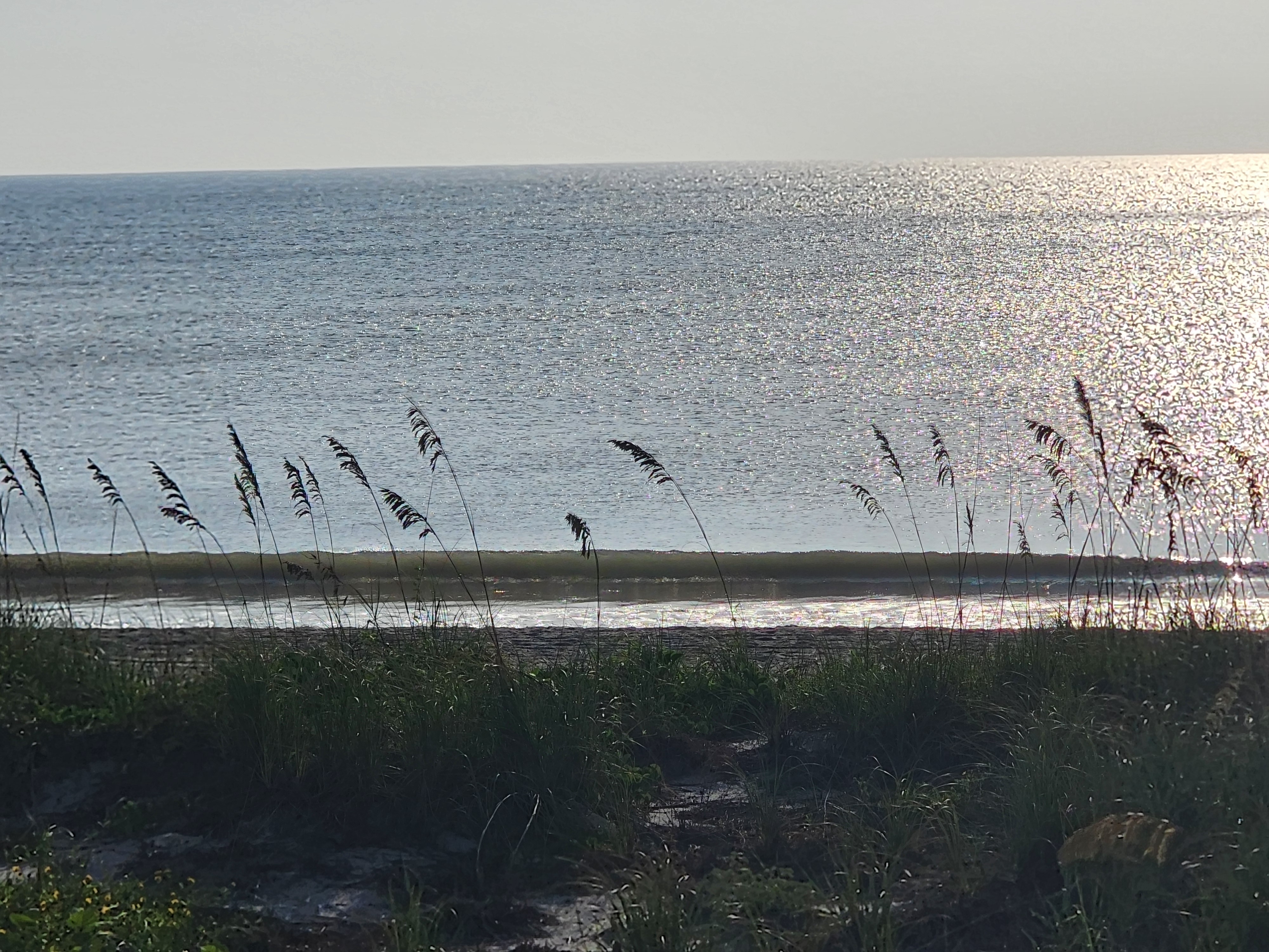 Small ripple breaking on the sand at high tide, backlit by sun glare, South Cocoa Beach