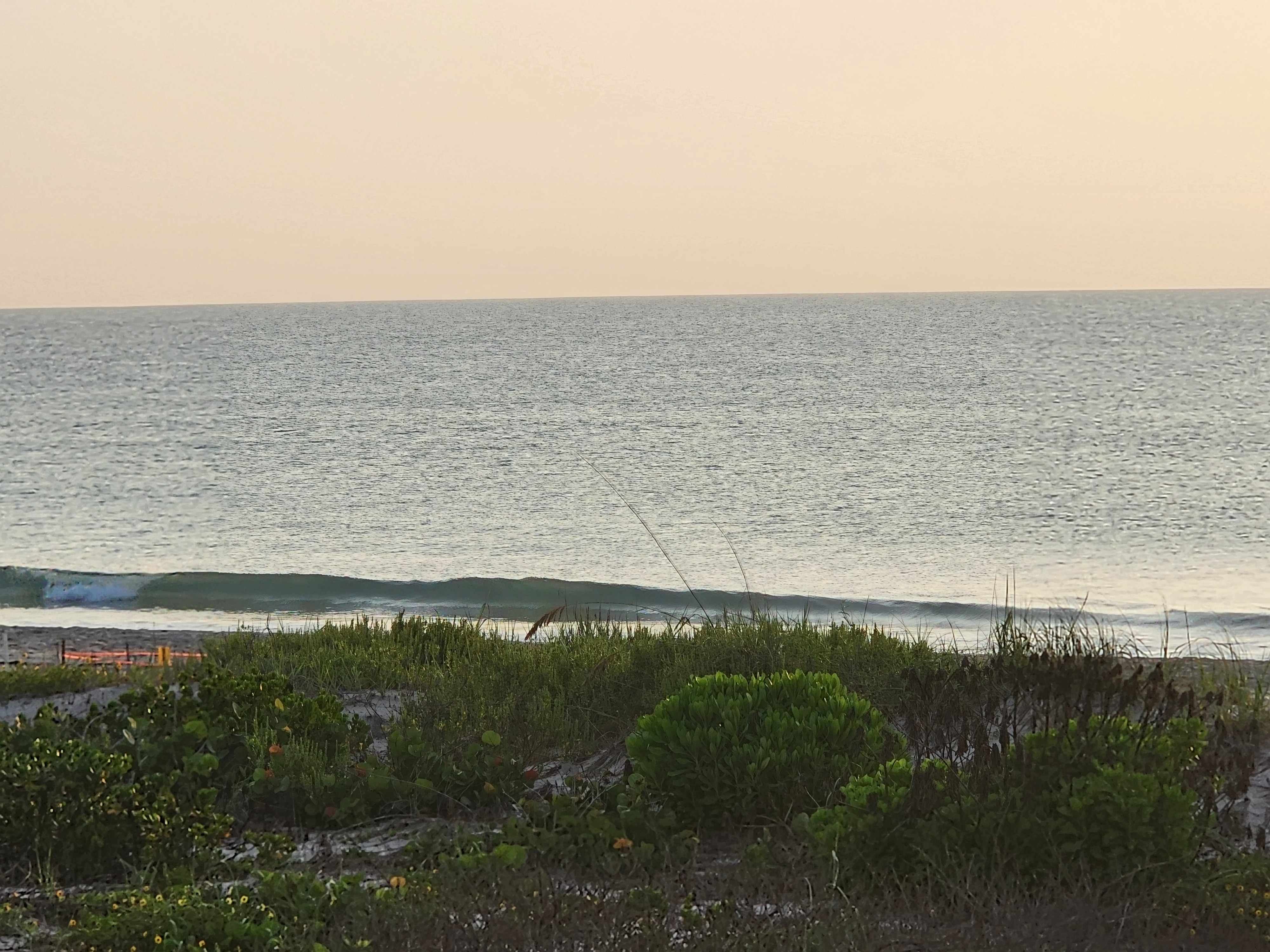 Small ripple breaking on the sand at high tide, backlit by sun glare, South Cocoa Beach