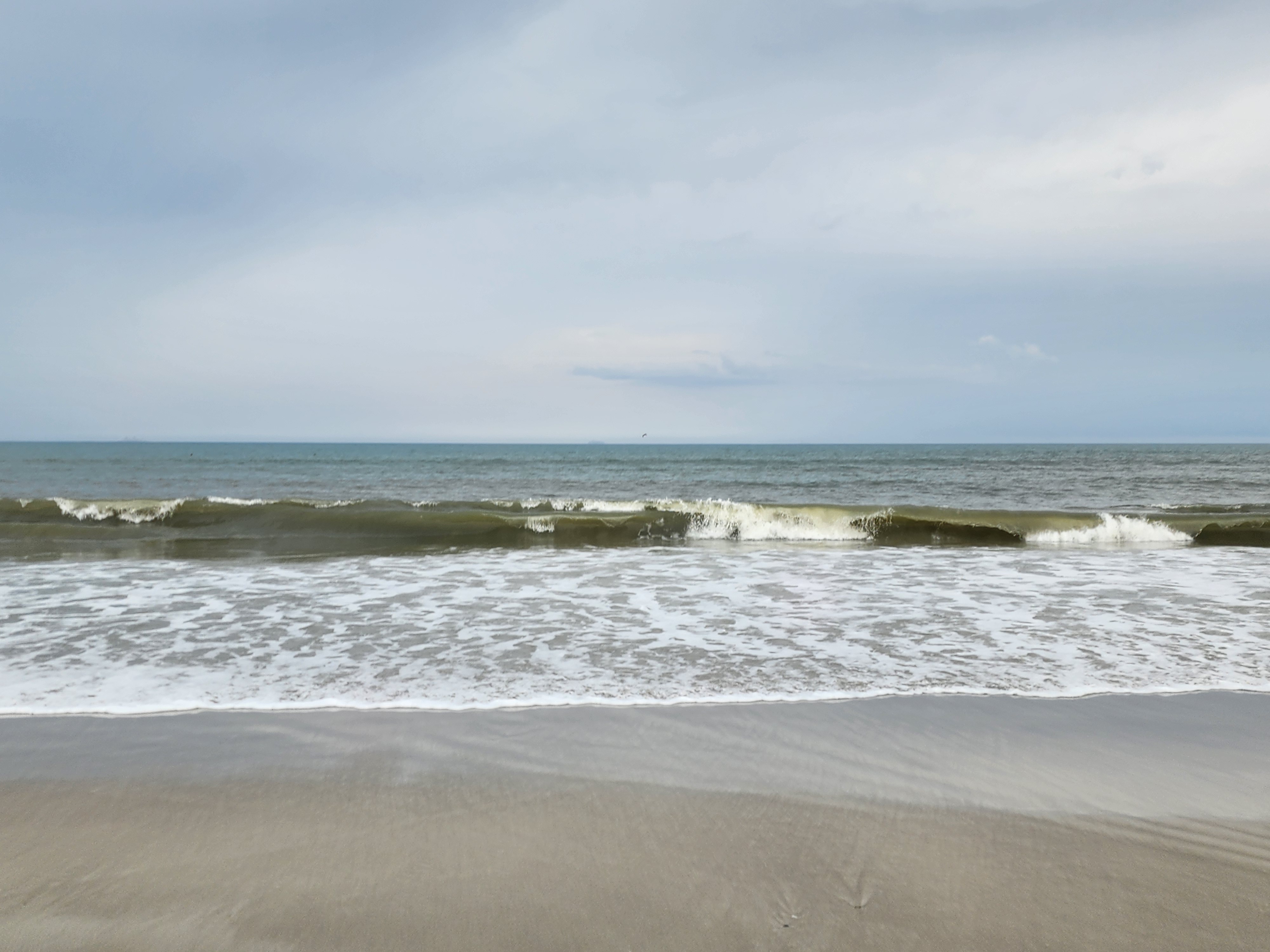 Close up of a small wave breaking onshore and washing up the wet sand under a cloudy sky