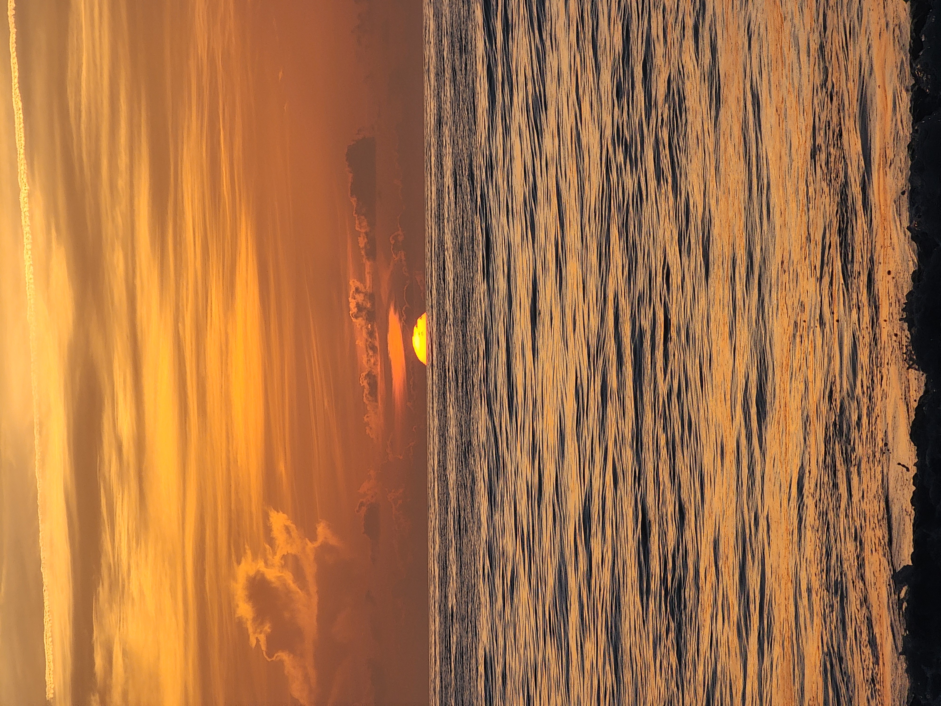 Sun cresting the horizon over the Atlantic in a deep orange sky, glassy swell lines rolling toward the beach at South Cocoa Beach