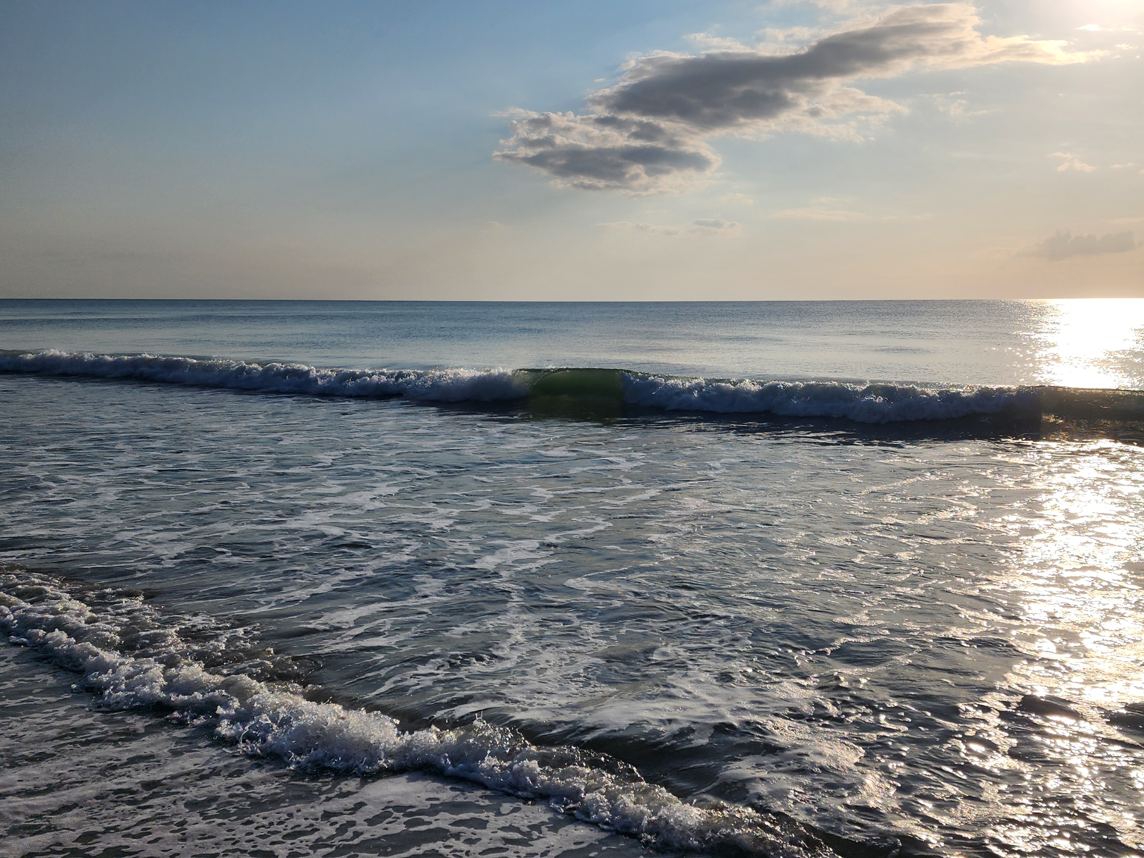 Sunlit shorebreak wave curling under scattered clouds, South Cocoa Beach