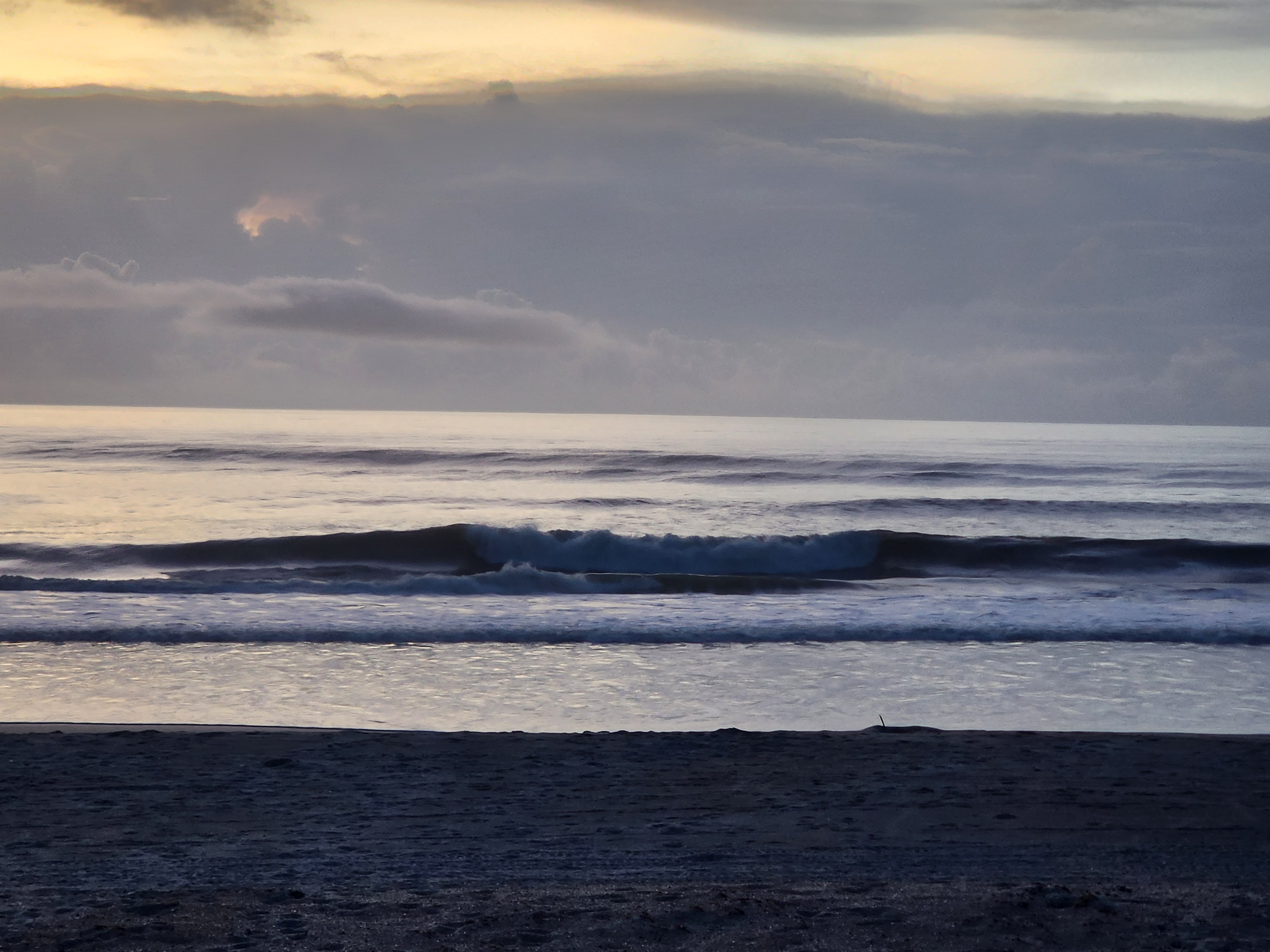 Empty beach in the foreground as a 3-4 foot set wave peels down the line at Picnic Tables, South Cocoa Beach