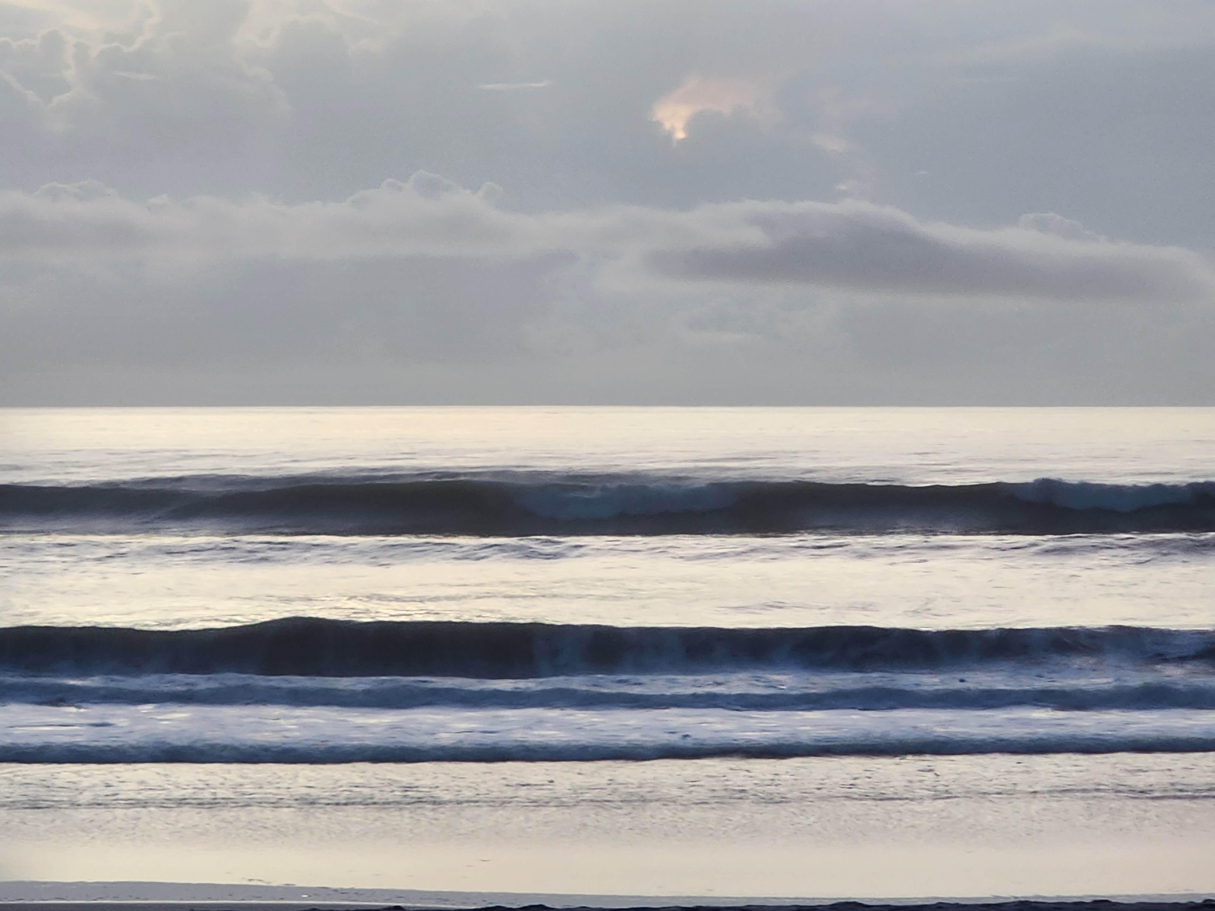 Two stacked lines of groundswell breaking on the outside bar under heavy morning cloud cover, South Cocoa Beach