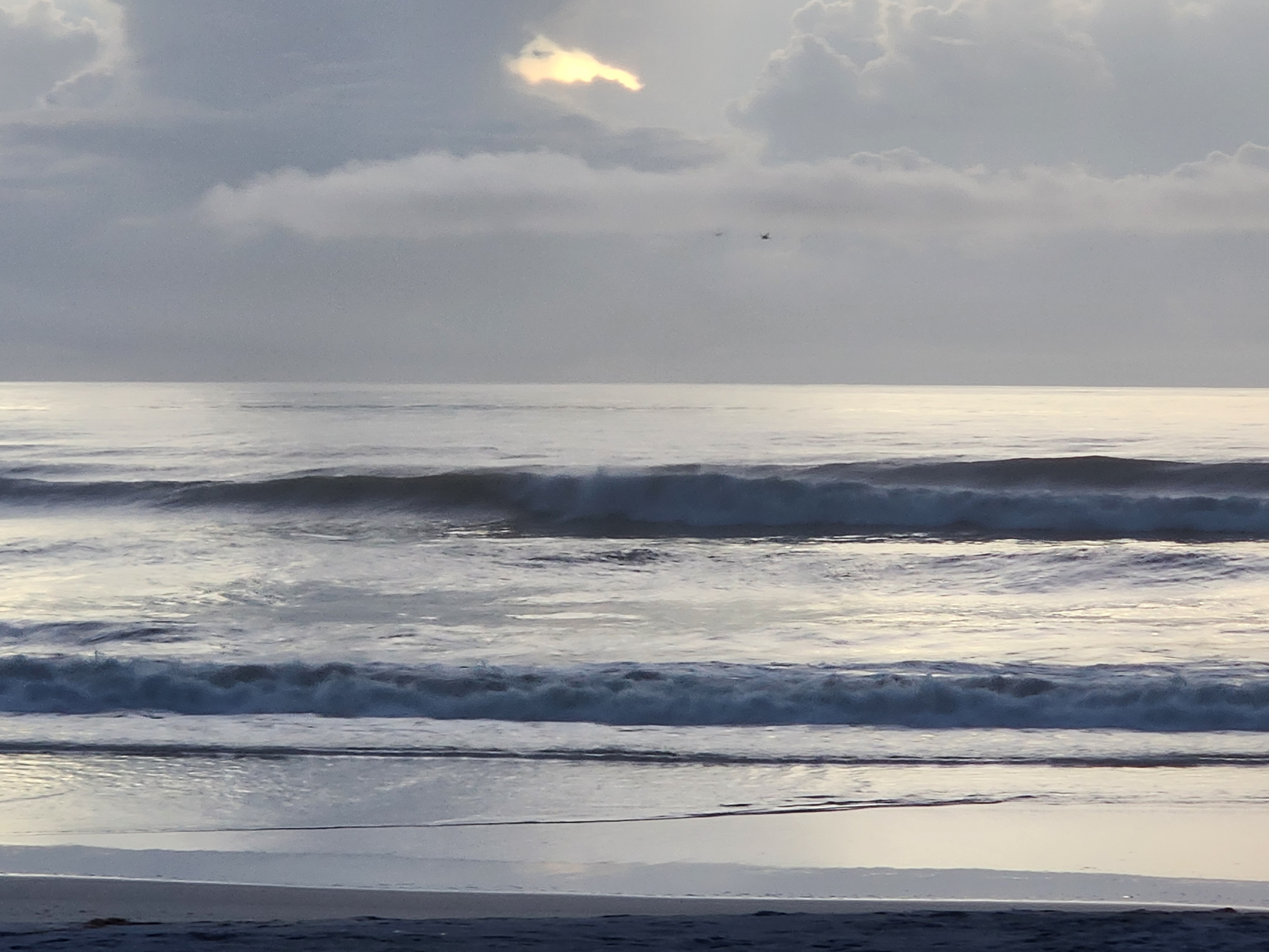 Wave breaking on the outside with the sun burning a hole through the clouds and birds working overhead, South Cocoa Beach