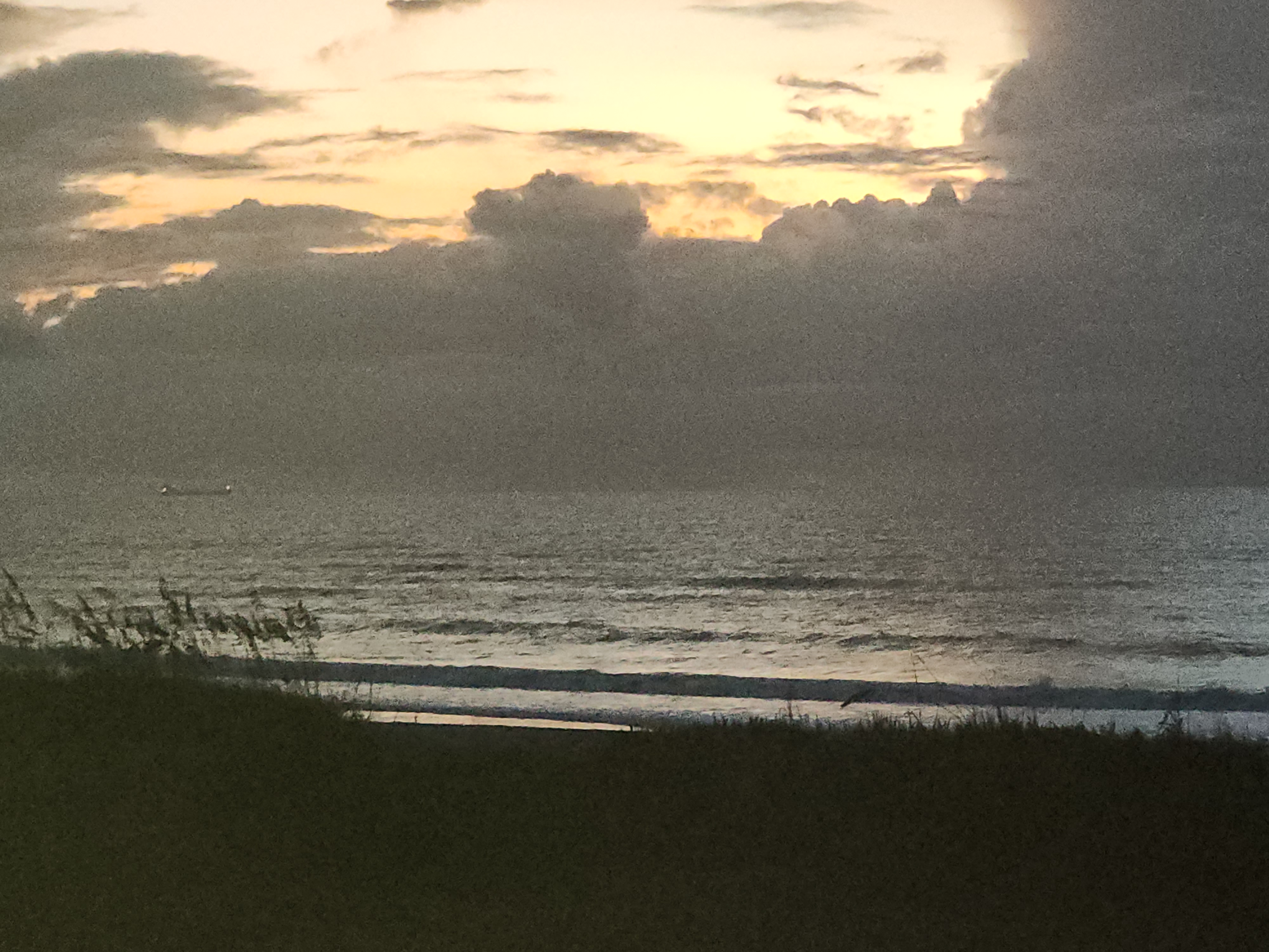 Pre-dawn sky glowing gold behind heavy cloud cover over a calm ocean, South Cocoa Beach