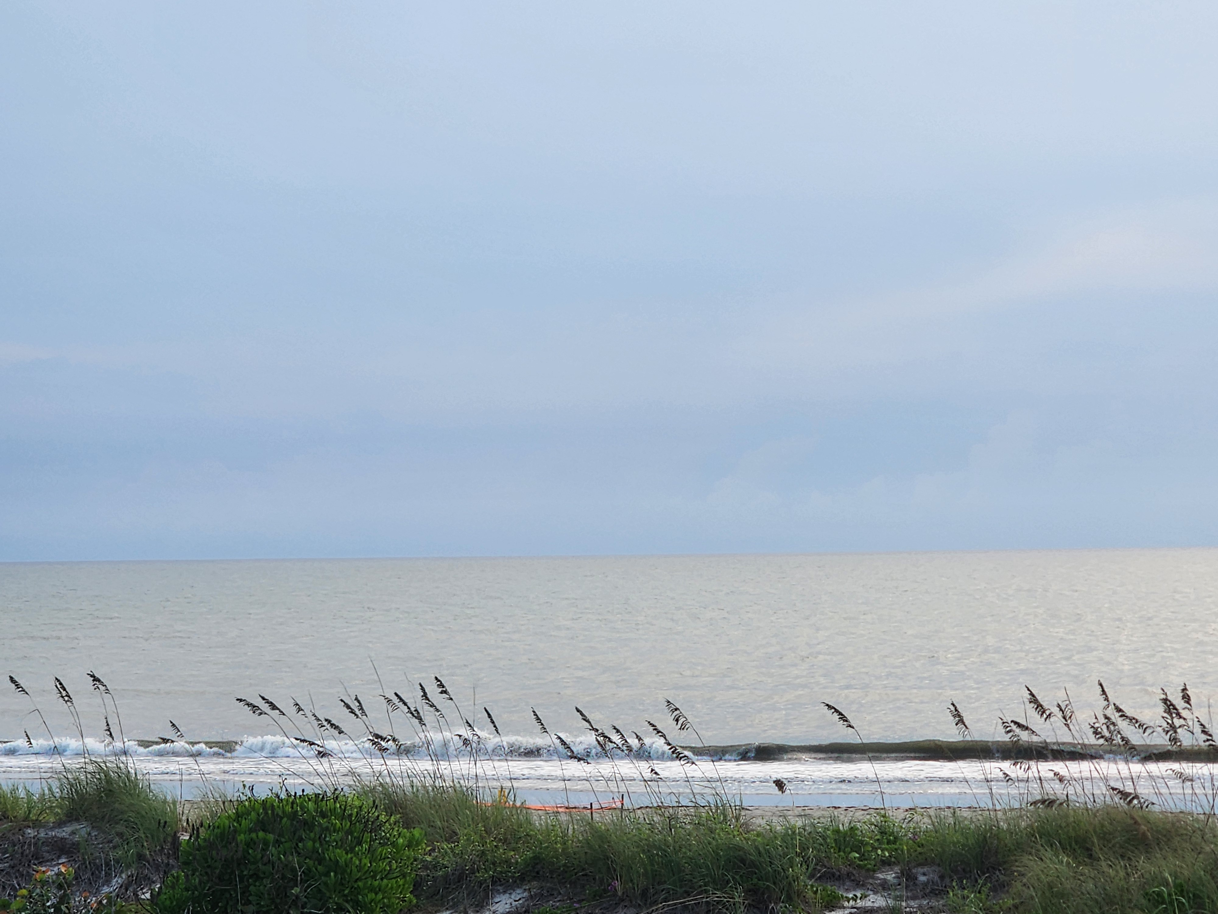 Small wind-blown 0-1 foot wave crumbling toward an empty beach under overcast skies at 32nd Street, South Cocoa Beach, September 2026