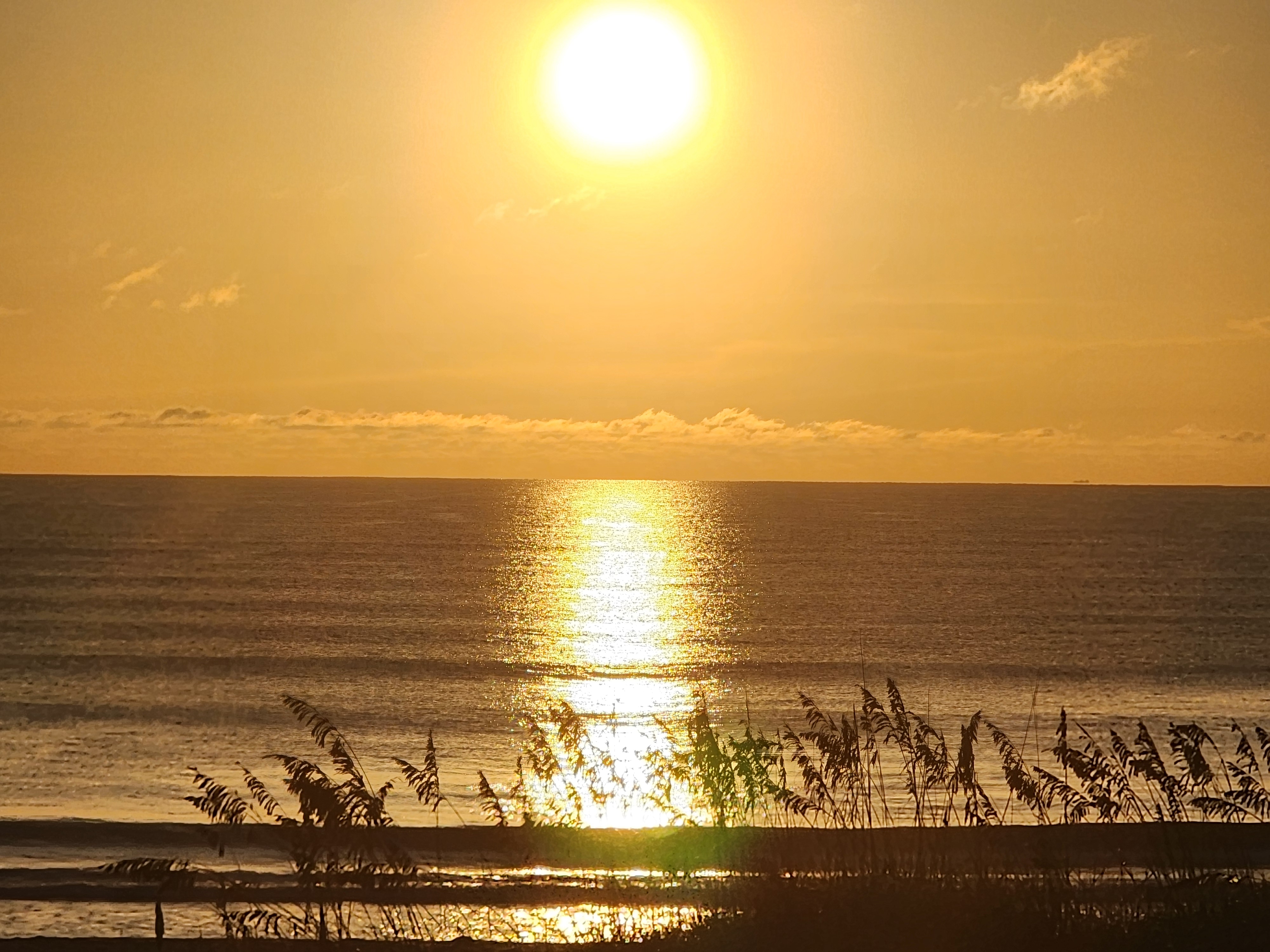 Golden sunrise burning over the Atlantic with a bright reflection down the water and sea oats silhouetted along the dune, 32nd Street, South Cocoa Beach, September 2026