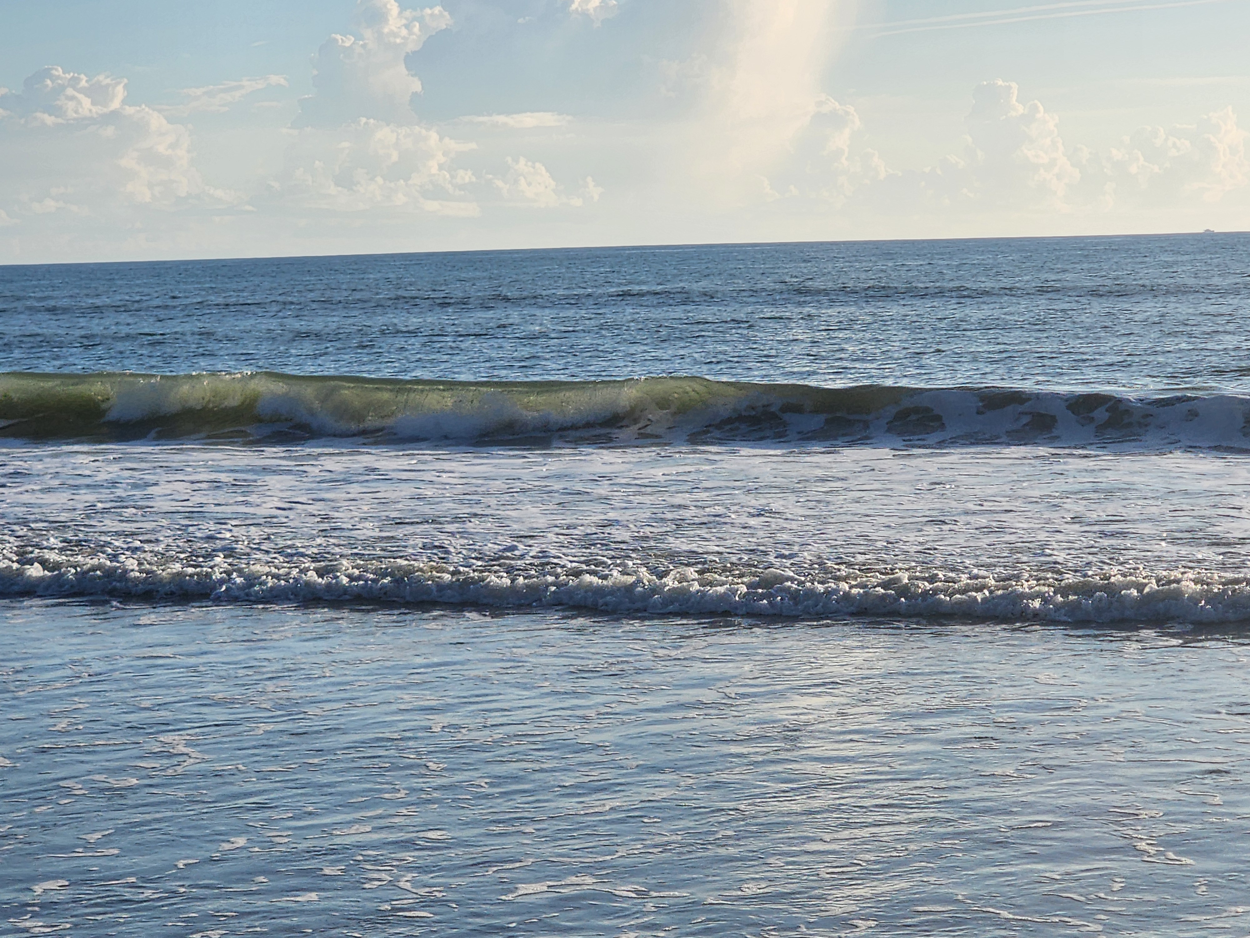 Close-up of a sunlit green wave face with light ESE bump on the water and whitewater reforming inside, cumulus clouds building offshore, South Cocoa Beach