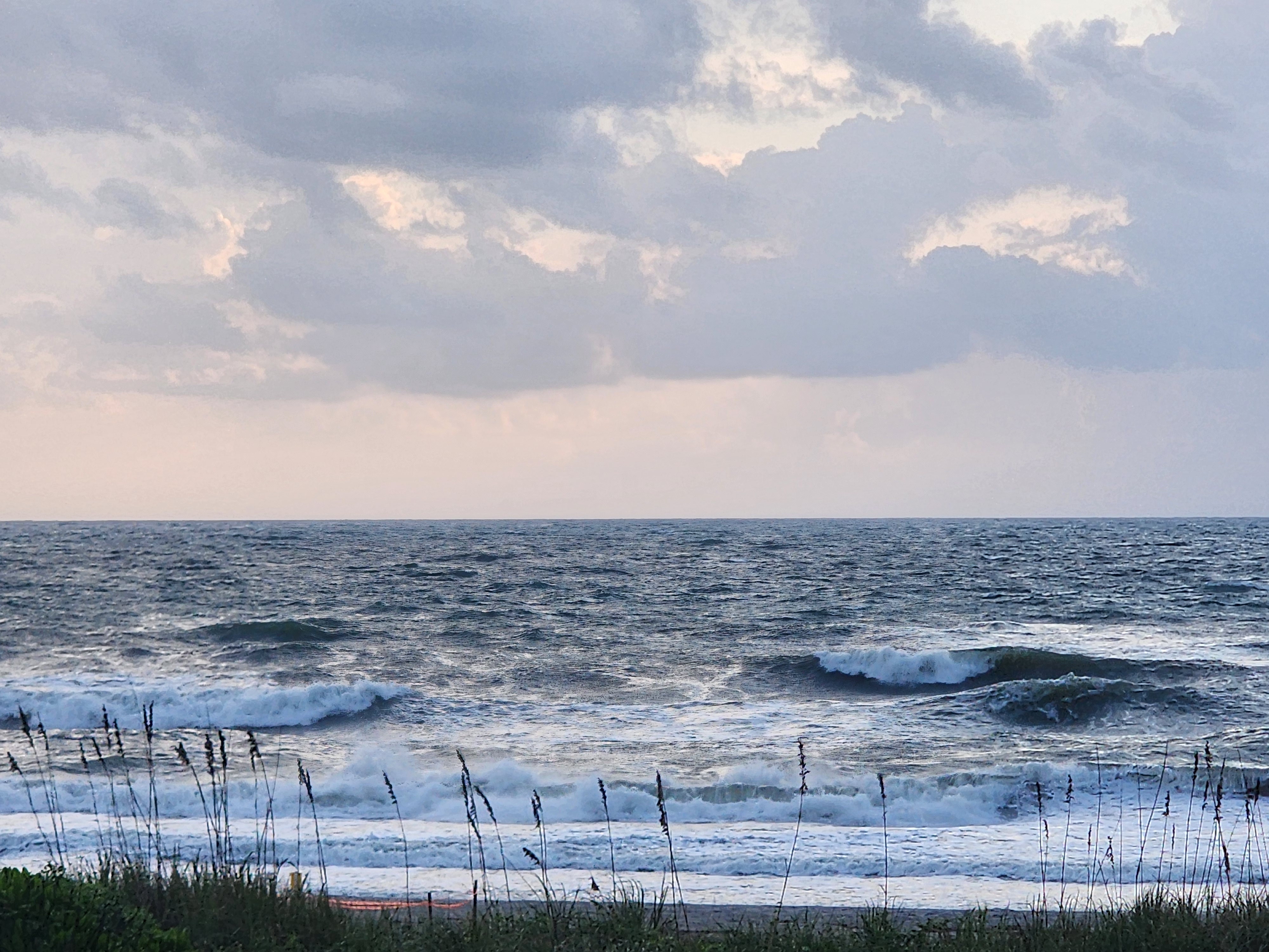 Pastel morning clouds over multiple lines of whitewater and wind chop, sea oats silhouetted in the foreground at South Cocoa Beach