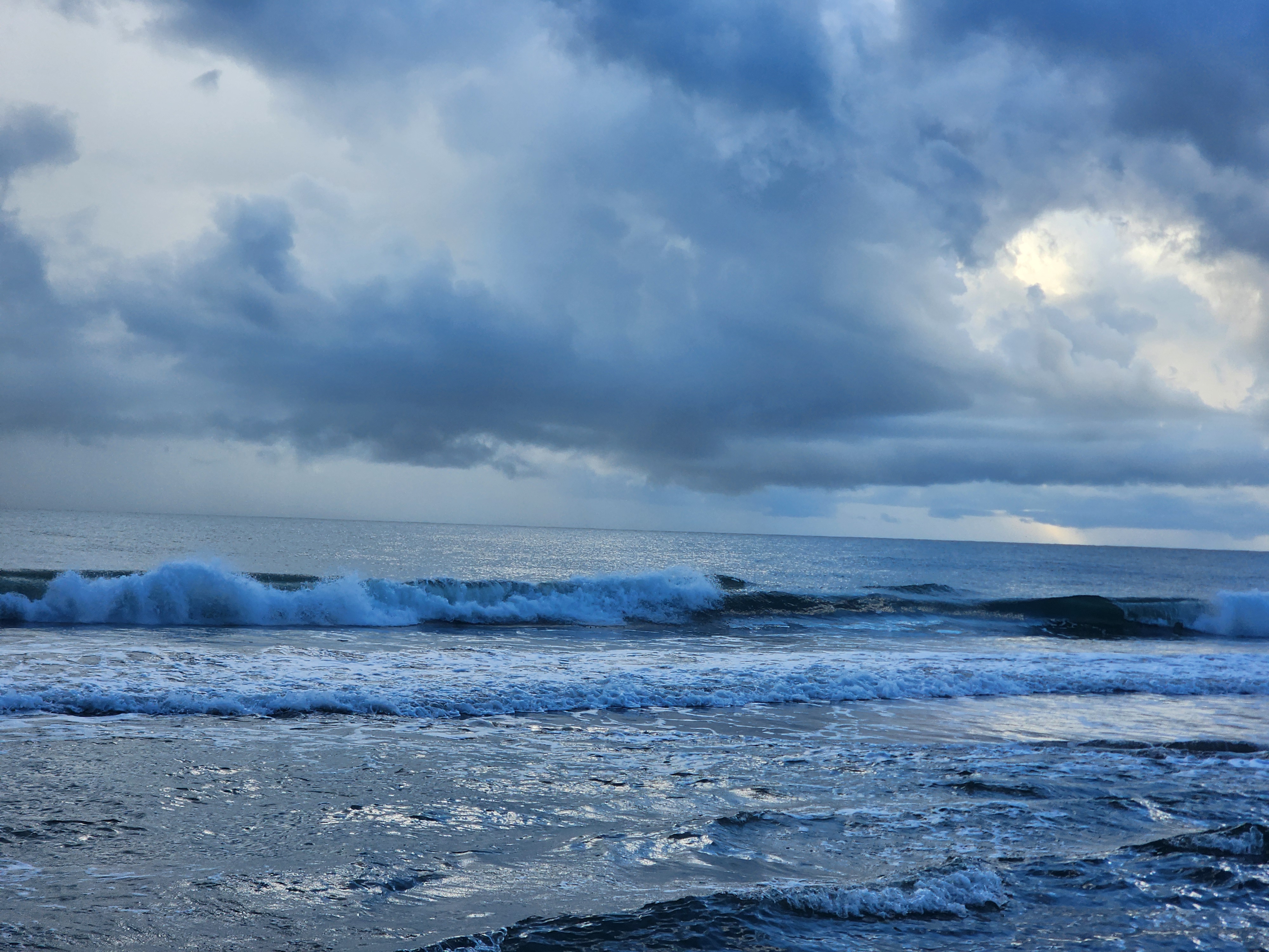 Knee to waist high wave breaking nearshore at Cocoa Beach under dark stormy skies with rain visible on the horizon