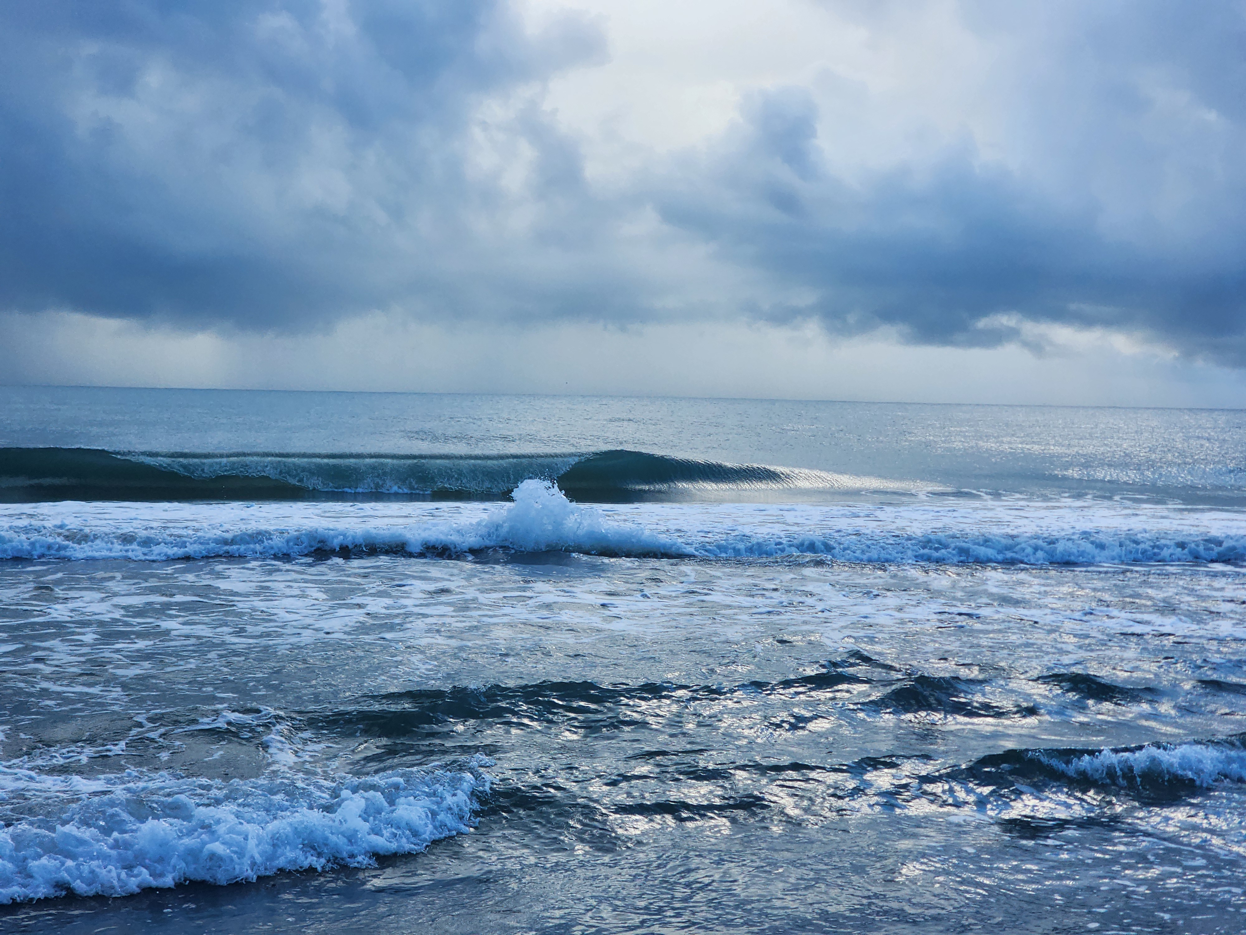 Glassy 1-2 ft longboard peeler with a clean open shoulder breaking nearshore at low tide in South Cocoa Beach on a stormy morning