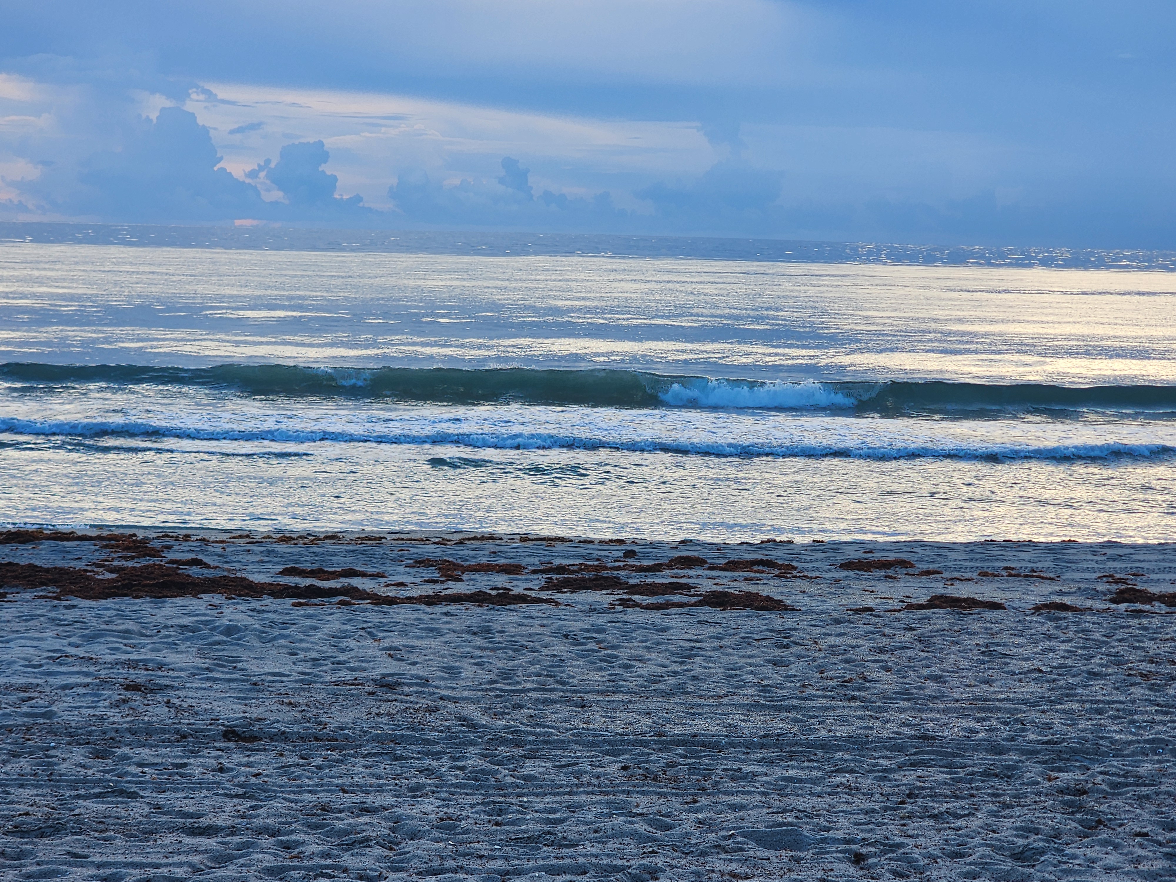 Clean little longboard wave peeling across glassy water at low tide in Cocoa Beach with cumulus clouds stacked on the horizon