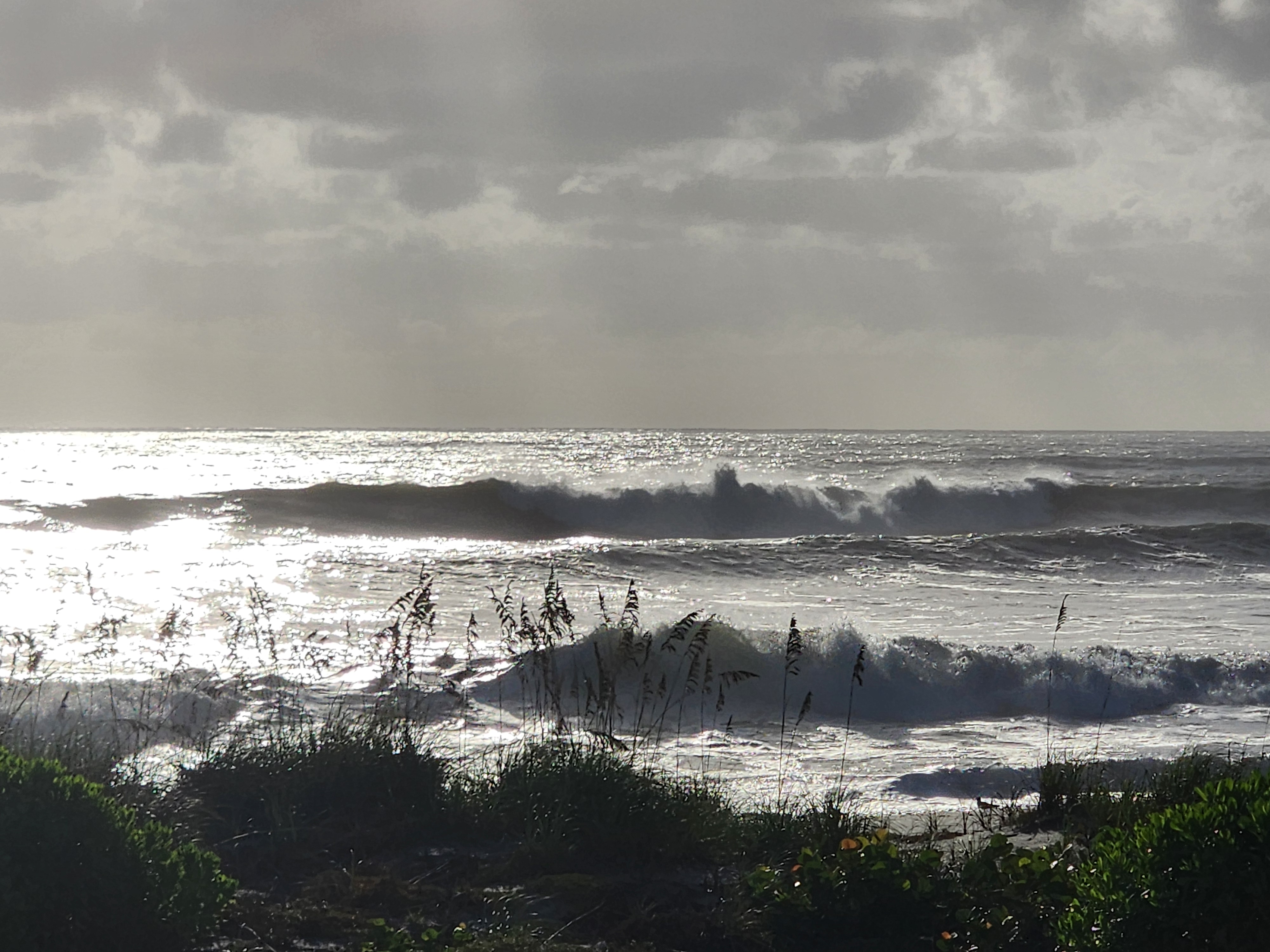 Silhouetted sets pitching with spray blowing off the lip under a moody overcast Cocoa Beach sky
