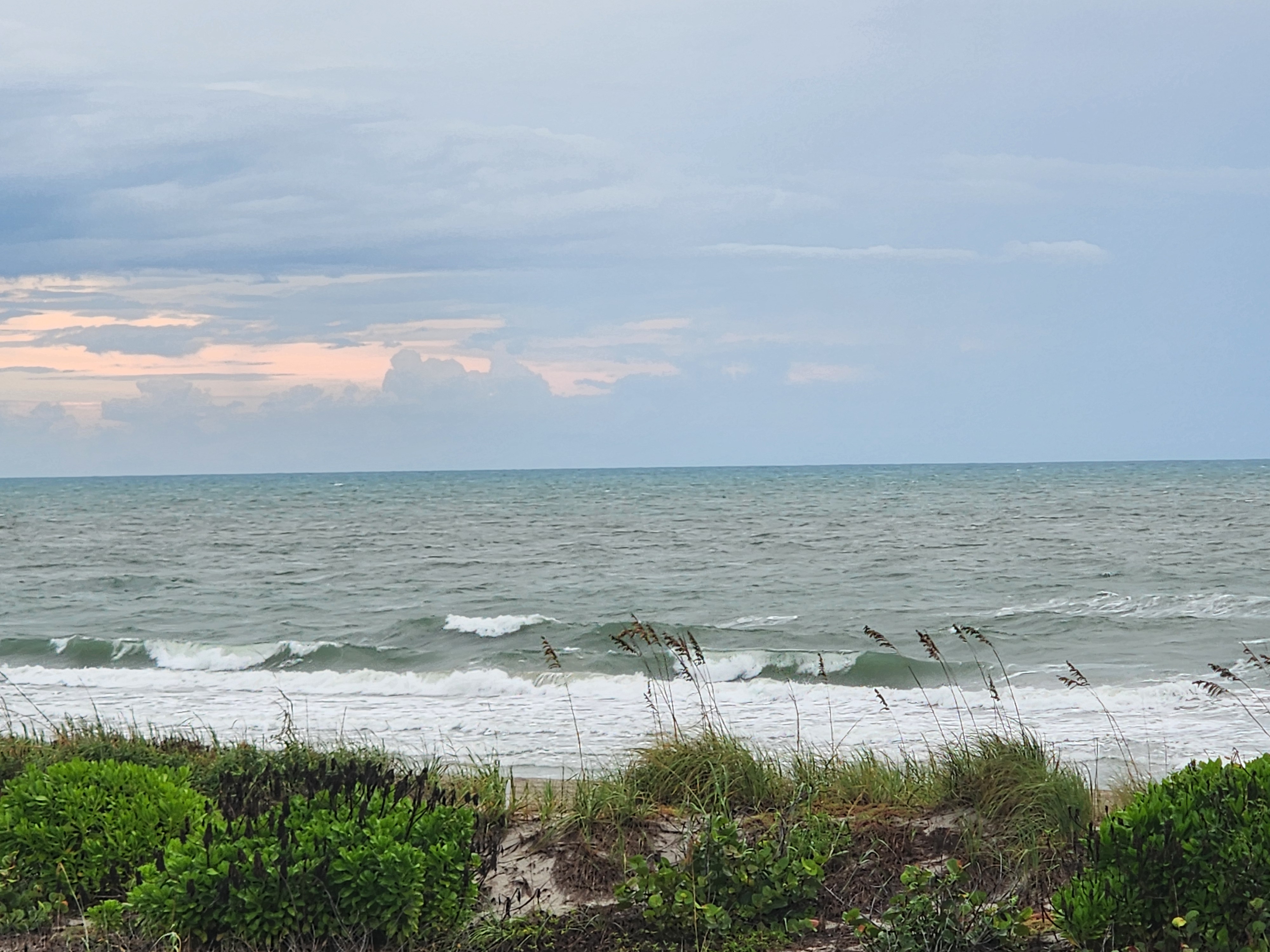 Short-period wind swell breaking close to shore beneath a gray sky with faint pink clouds